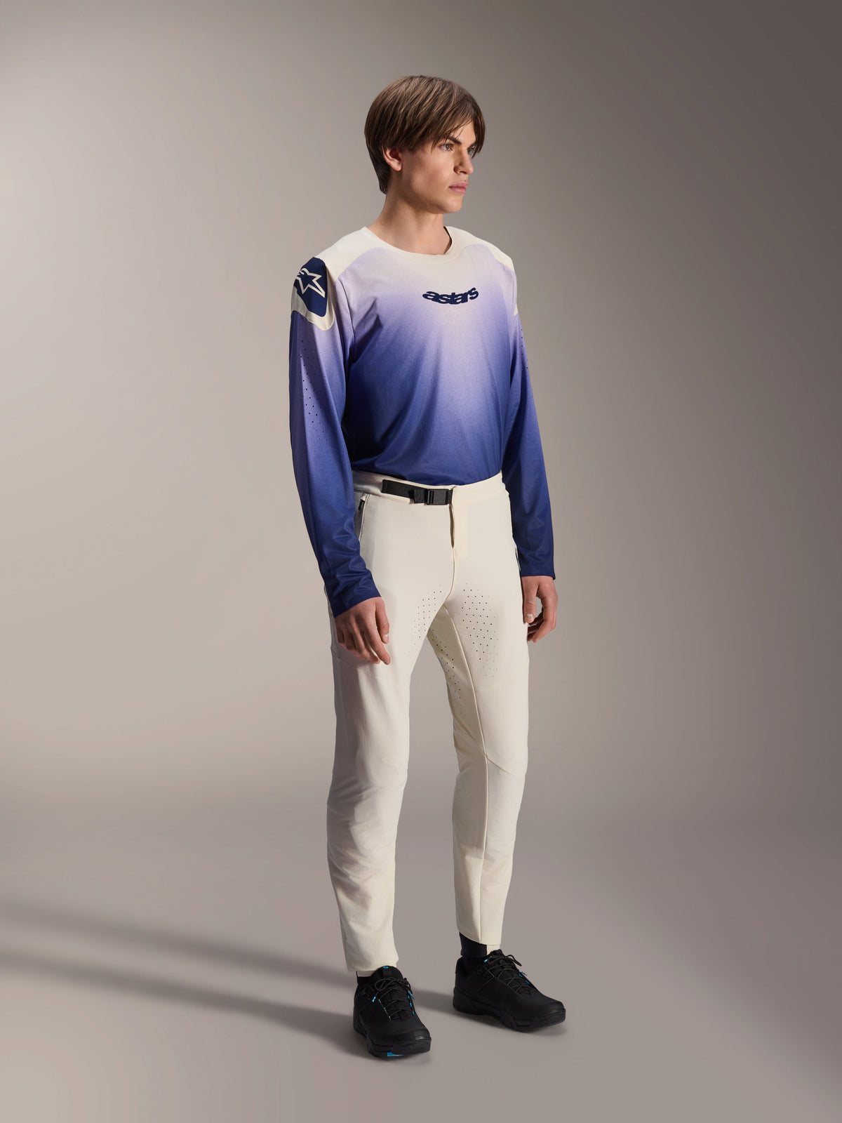 Alpinestars A-Aria Polartec Maker Elite-tröja i Baja Blue, långärmad mountainbiketröja med vit-till-blå gradientdesign och svart 'astars'-logotyp på bröstet, matchad med off-white mountainbikebyxor och svarta skor, MTB-utrustning med prestandapassform för stigcykling