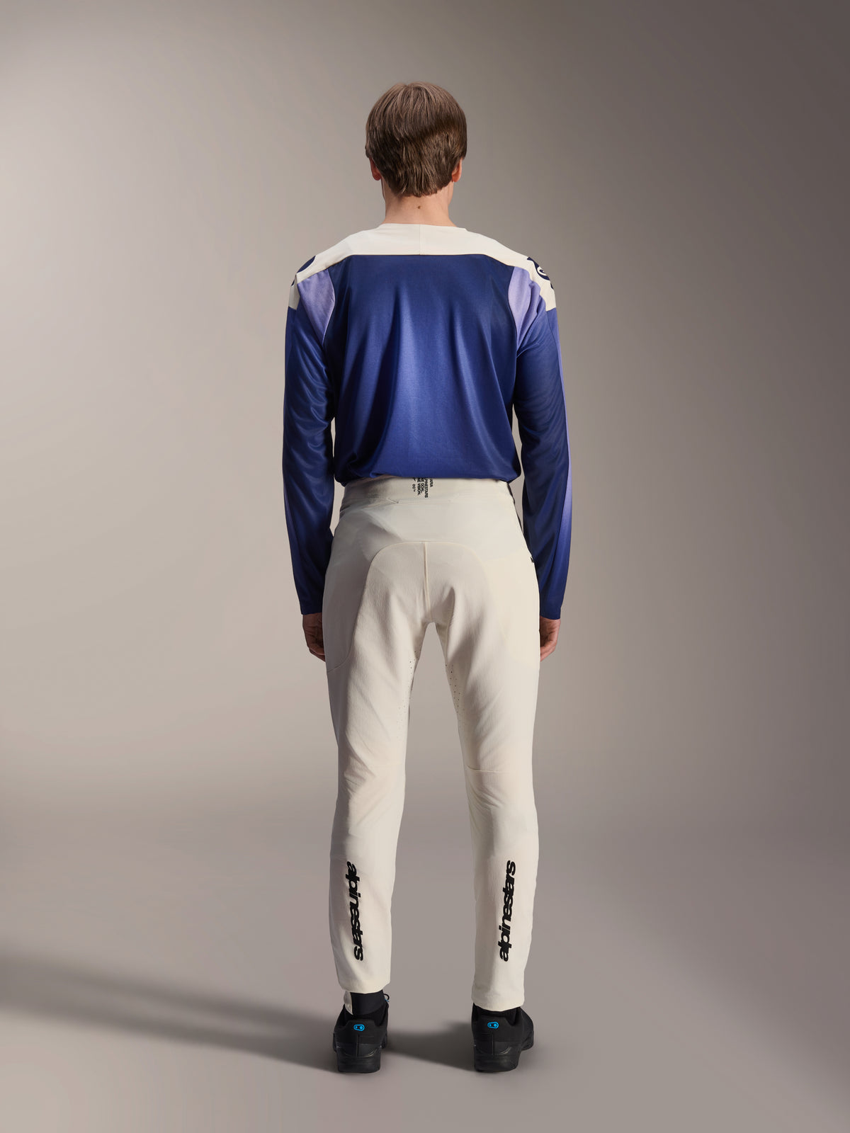Alpinestars A-Aria Elite-byxor i Ecru, sedda bakifrån på en modell tillsammans med en blå A-Aria Polartec Maker Elite långärmad tröja, benvita tekniska MTB-byxor med svarta logotyper på underbenen, prestandautrustning för mountainbike