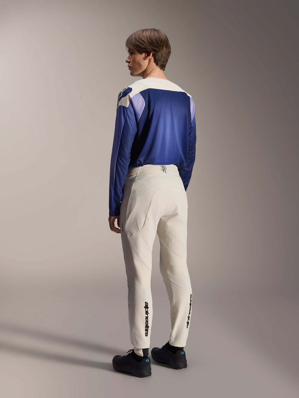 Alpinestars A-Aria Polartec Maker Elite långärmad tröja, Baja Blue, bärs av en manlig modell bakifrån med benvita MTB-byxor och svarta skor, med en blå och vit färgblockerad design, prestandautrustning för mountainbike