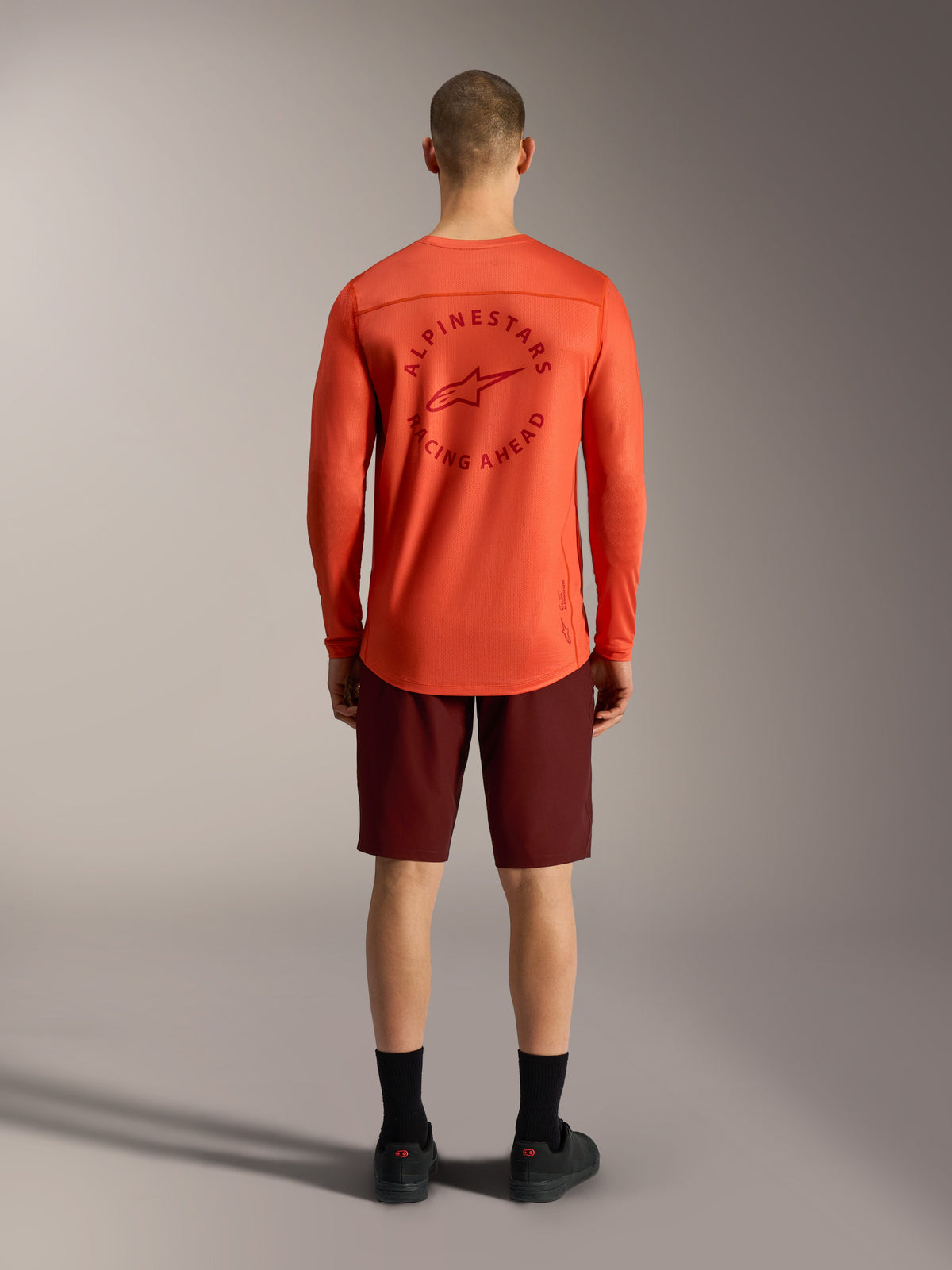 Orange A-Dura Air LS-tröja matchad med bordeauxfärgade Ride-shorts, vy bakifrån av Alpinestars MTB-funktionskläder.