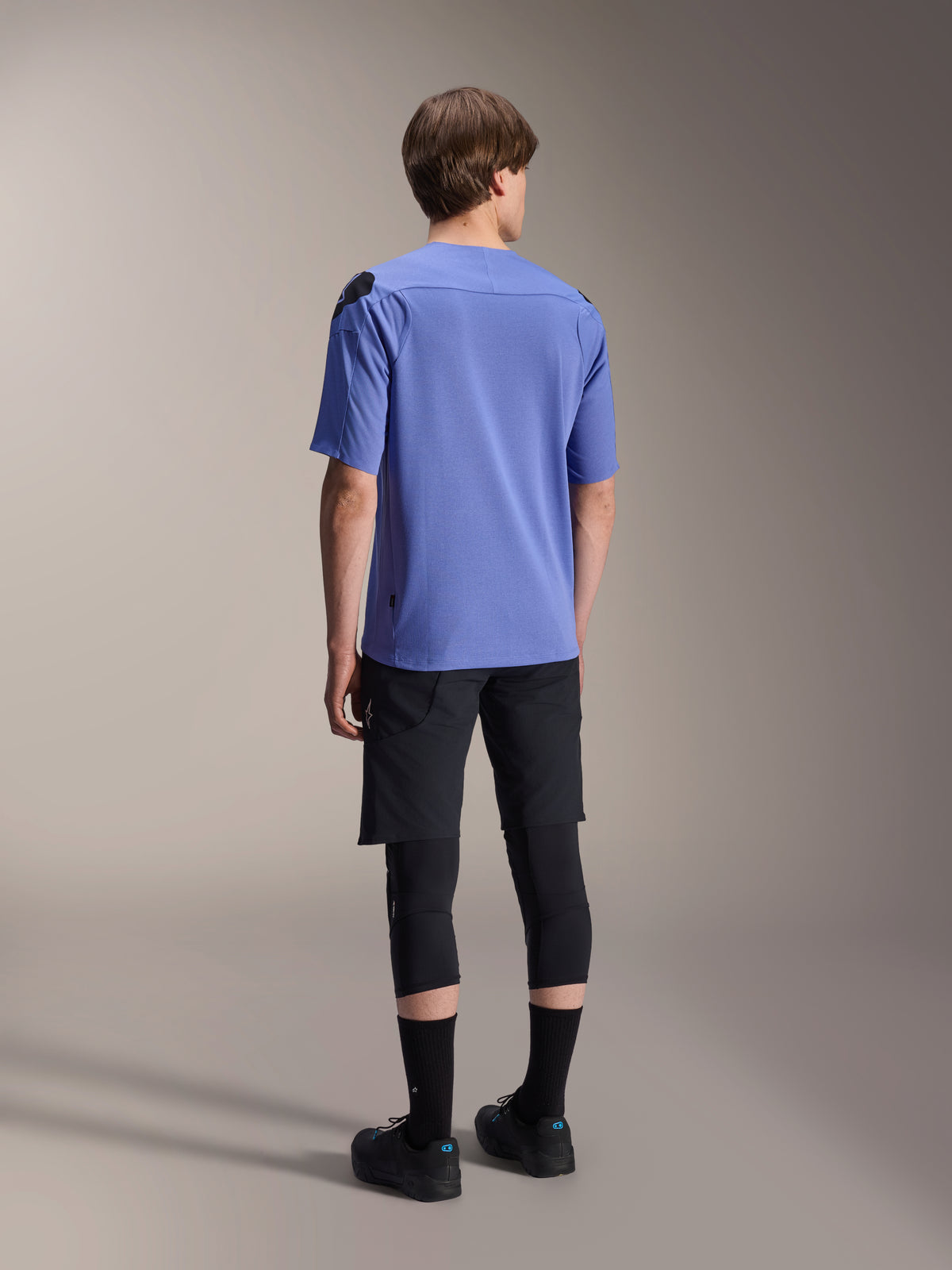 Alpinestars A-Aria Lite Short, Black mountain bike shorts, paired with a blue A-Aria Polartec Elite short-sleeve jersey and black knee pads, back view of a rider in performance cycling gear for off-road trails.