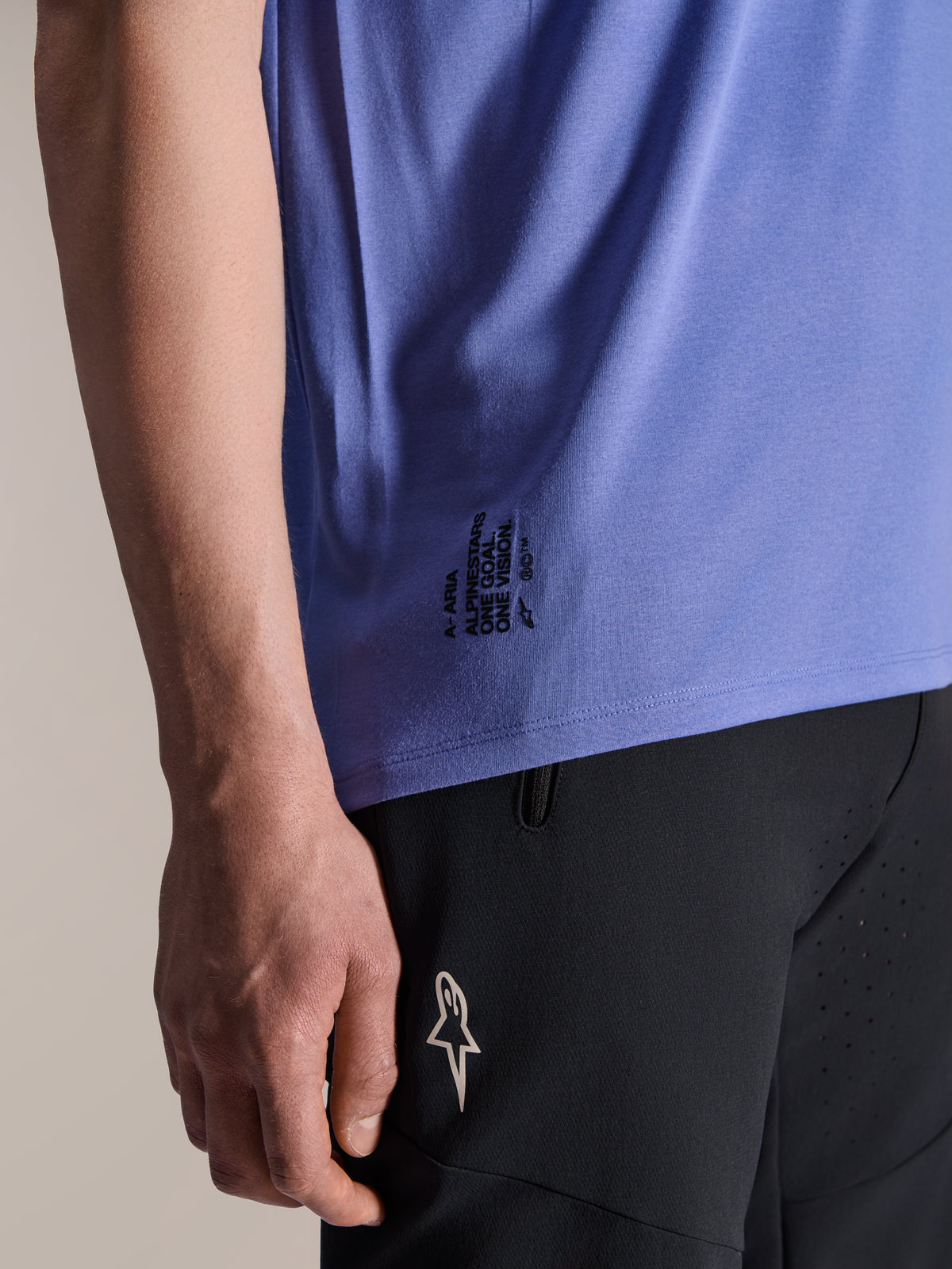 Alpinestars A-Aria Polartec Elite Short Sleeve Jersey in Baja Blue, detail of the lower side hem featuring black 'One Goal. One Vision.' text and ASTARS logo branding, paired with black mountain bike shorts.