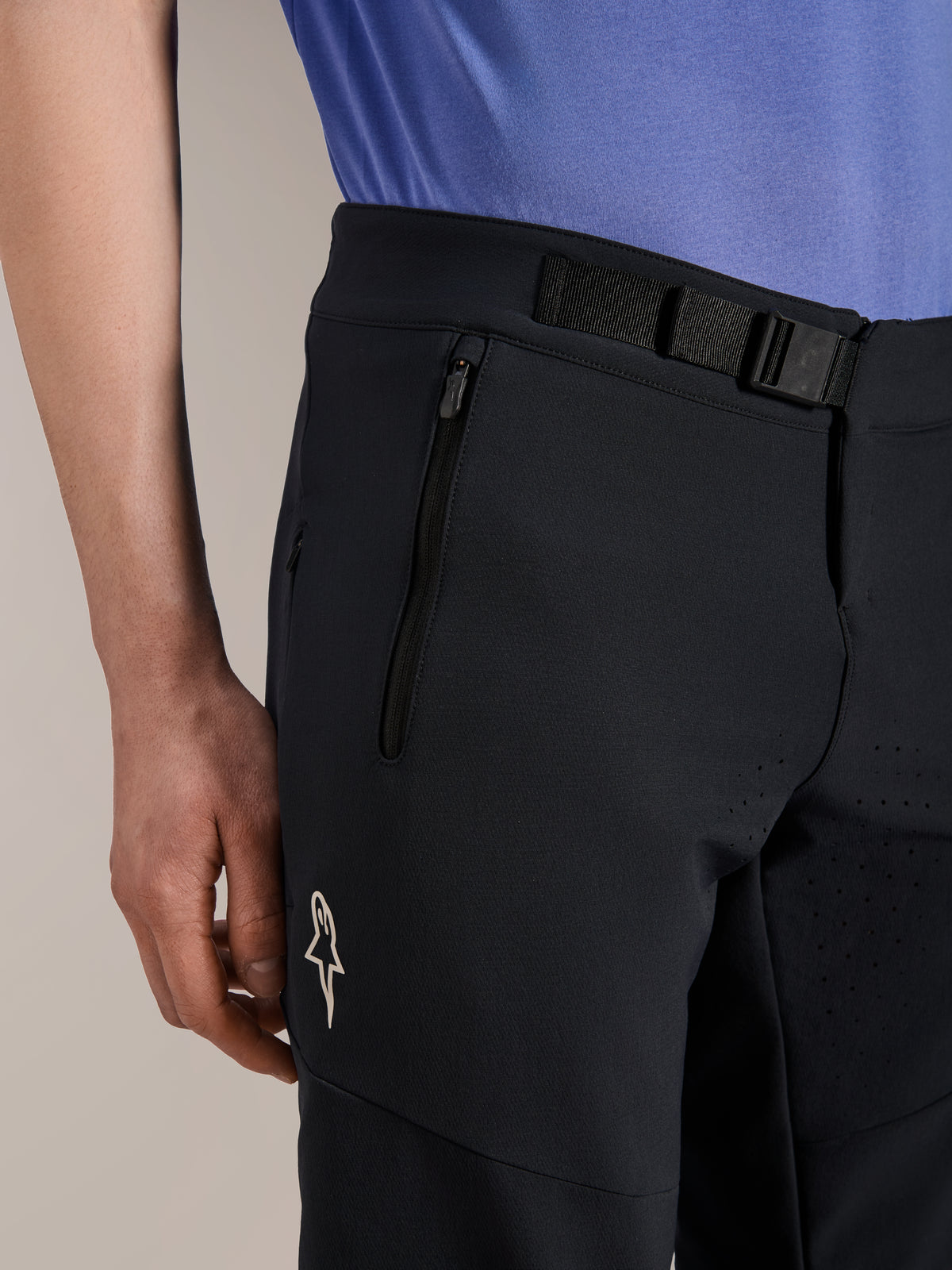 Alpinestars A-Aria Elite Shorts, Mountain Bike Shorts, Black Titanium, featuring a magnetic buckle closure, zippered pocket, and white Alpinestars logo, worn with a blue cycling jersey, performance mountain bike gear