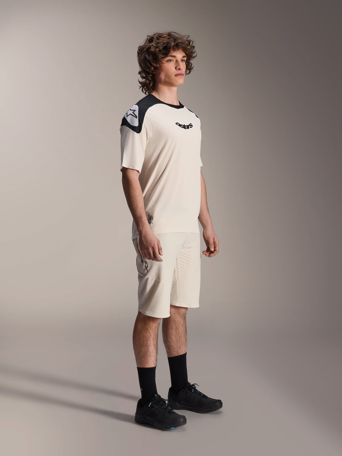 Alpinestars A-Aria Polartec Elite Short Sleeve Jersey, Ecru with black shoulder panels and logo, worn by a model with matching shorts and black shoes, performance mountain bike apparel for off-road trail riding.