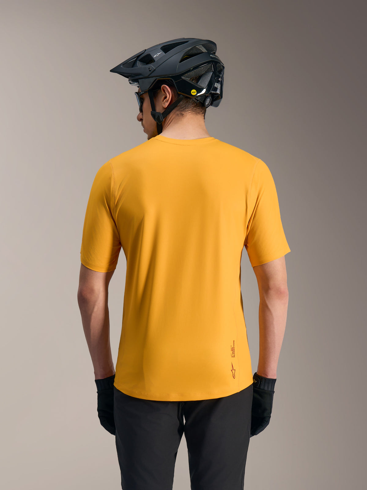 Orange A-Dura Ride kortärmad MTB-tröja, lättviktstopp sedd bakifrån med logotyp, förlängt bakstycke och svart hjälm.