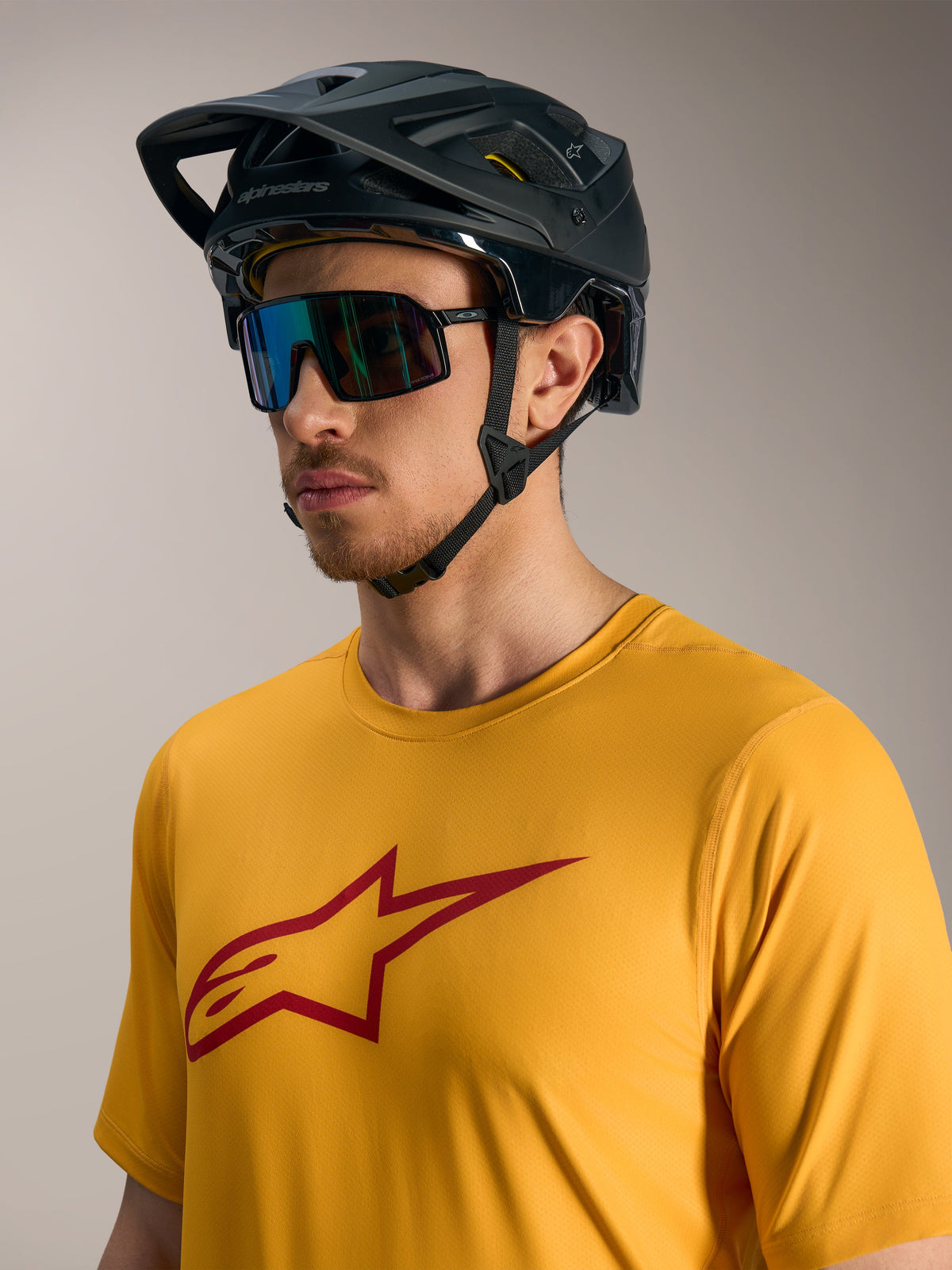 Orange A-Dura Ride kortärmad tröja med röd Astars-logo, matchad med svart MTB-hjälm och sportglasögon.