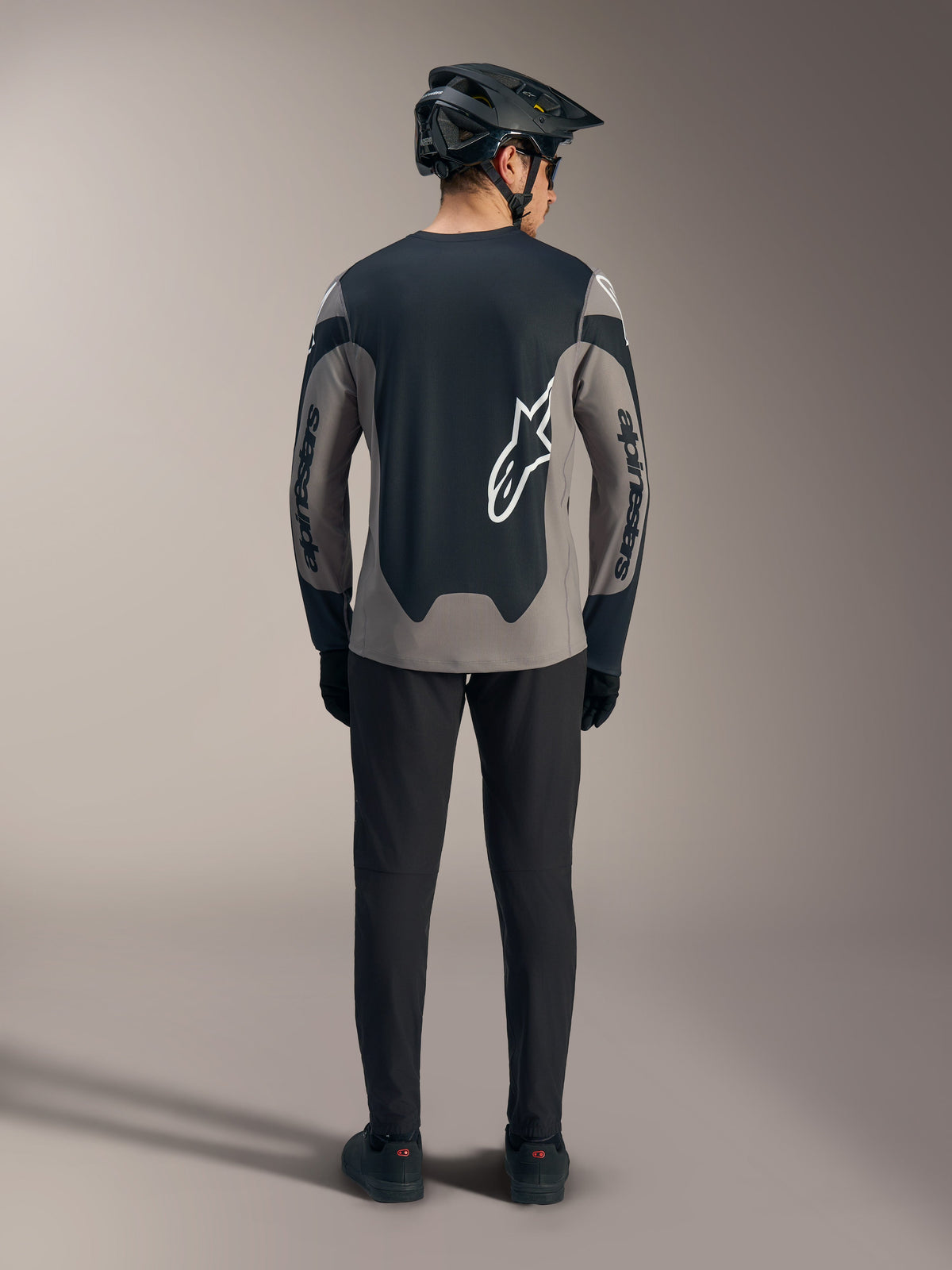 Grå A-Dura Race långärmad MTB-tröja sedd bakifrån, med svarta paneler och vita Alpinestars-logotyper.