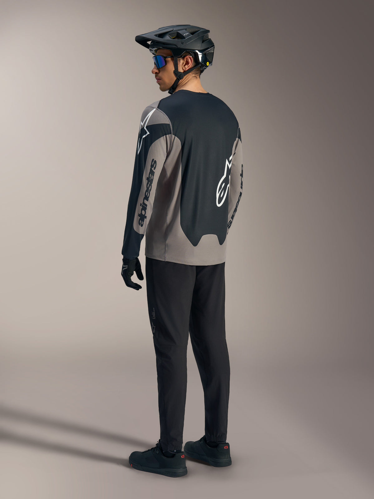 Grå och svart A-Dura Race långärmad tröja med Alpinestars-logotyper, sedd bakifrån i en komplett MTB-outfit.
