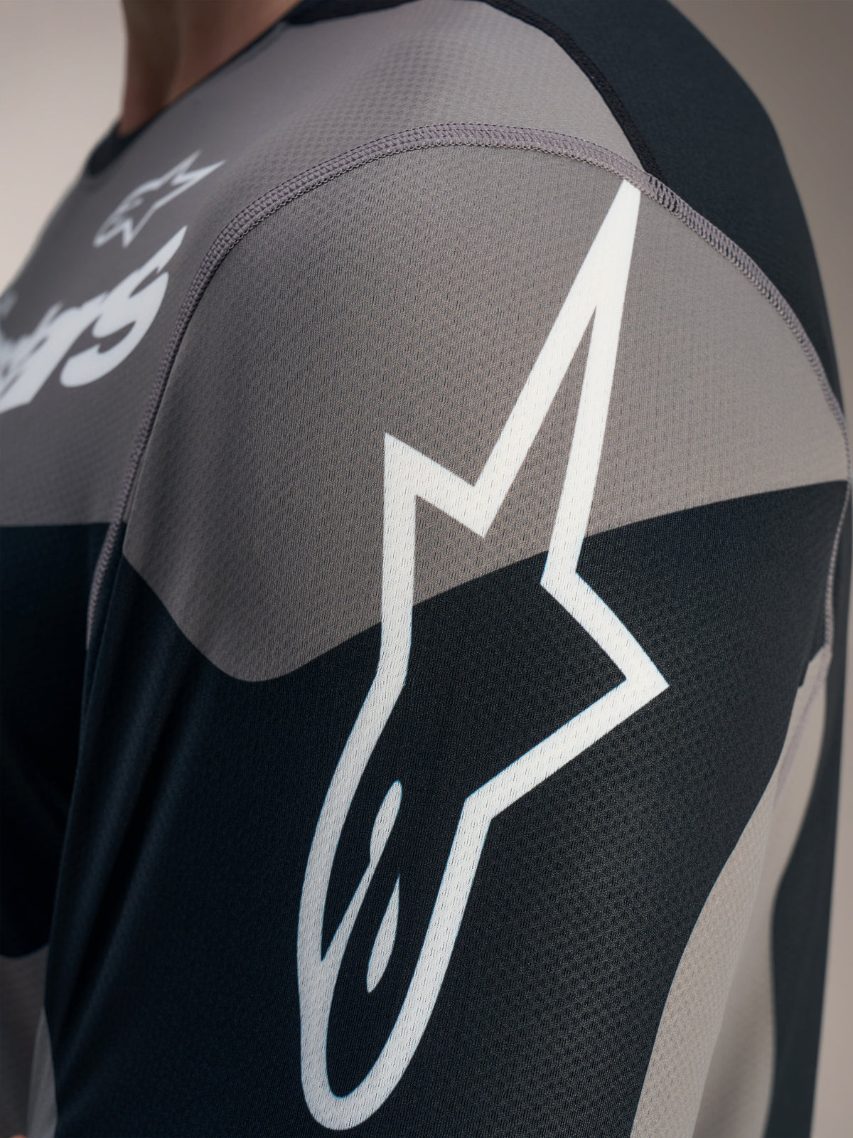 Grå A-Dura Race långärmad tröja, detalj med vit Astars-logotyp på texturerat tekniskt jacquard-meshtyg.