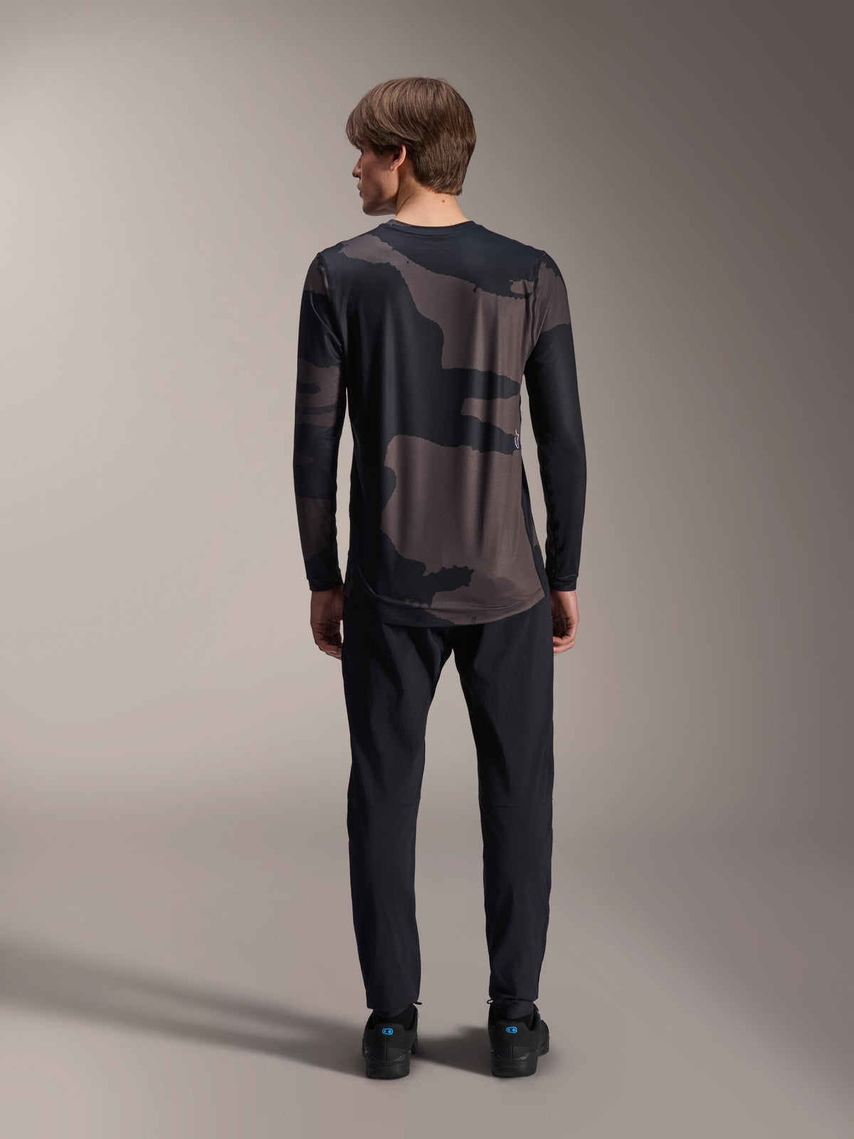 Alpinestars A-Dura Hollow Camo långärmad tröja, Black Camo, baksida buren med svarta byxor, med ett mörkt kamouflagemönster och förlängd rygg för MTB-täckning.