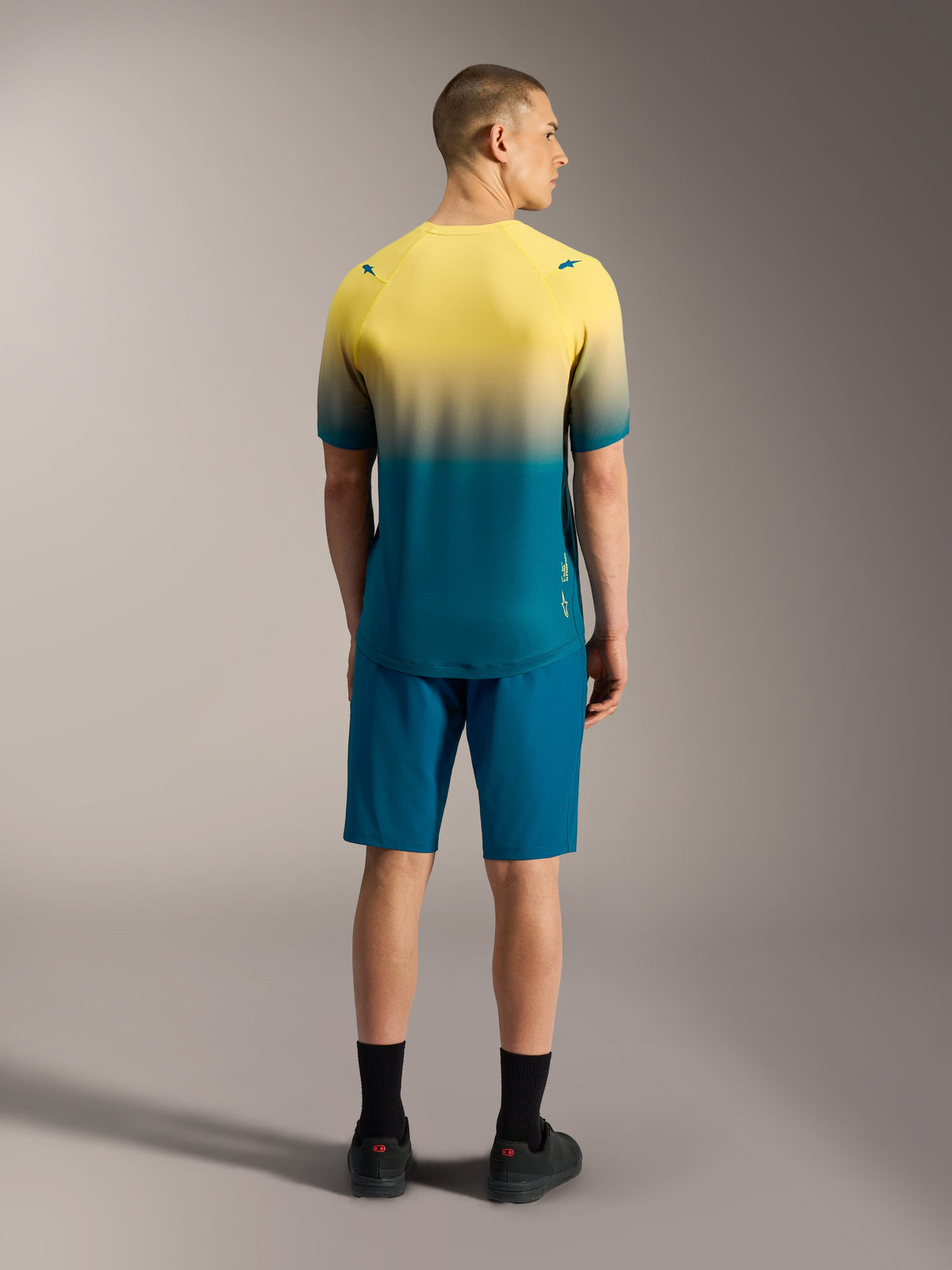 A-Dura ASTARS Jersey 2.0, kortärmad MTB-tröja med gul till blågrön gradient, visad bakifrån på en modell.