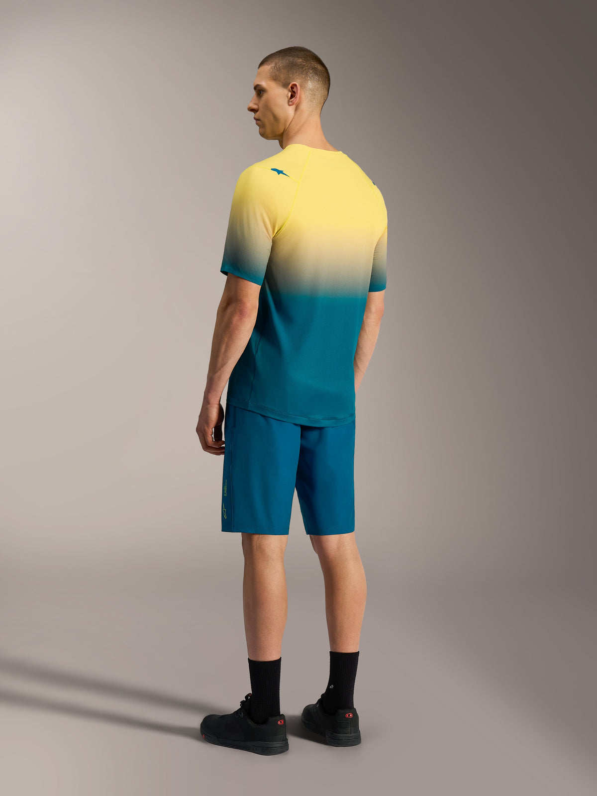 A-Dura ASTARS 2.0 kortärmad MTB-tröja i gul och turkos gradient, matchad med blå funktionsshorts.