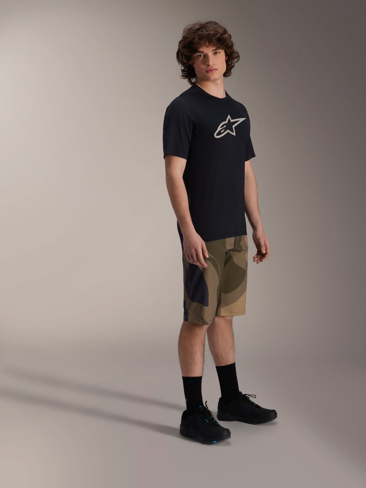 Alpinestars A-Dura Astar Short Sleeve Jersey, Black with white chest logo, worn with camouflage shorts and black MTB shoes, casual mountain bike riding gear