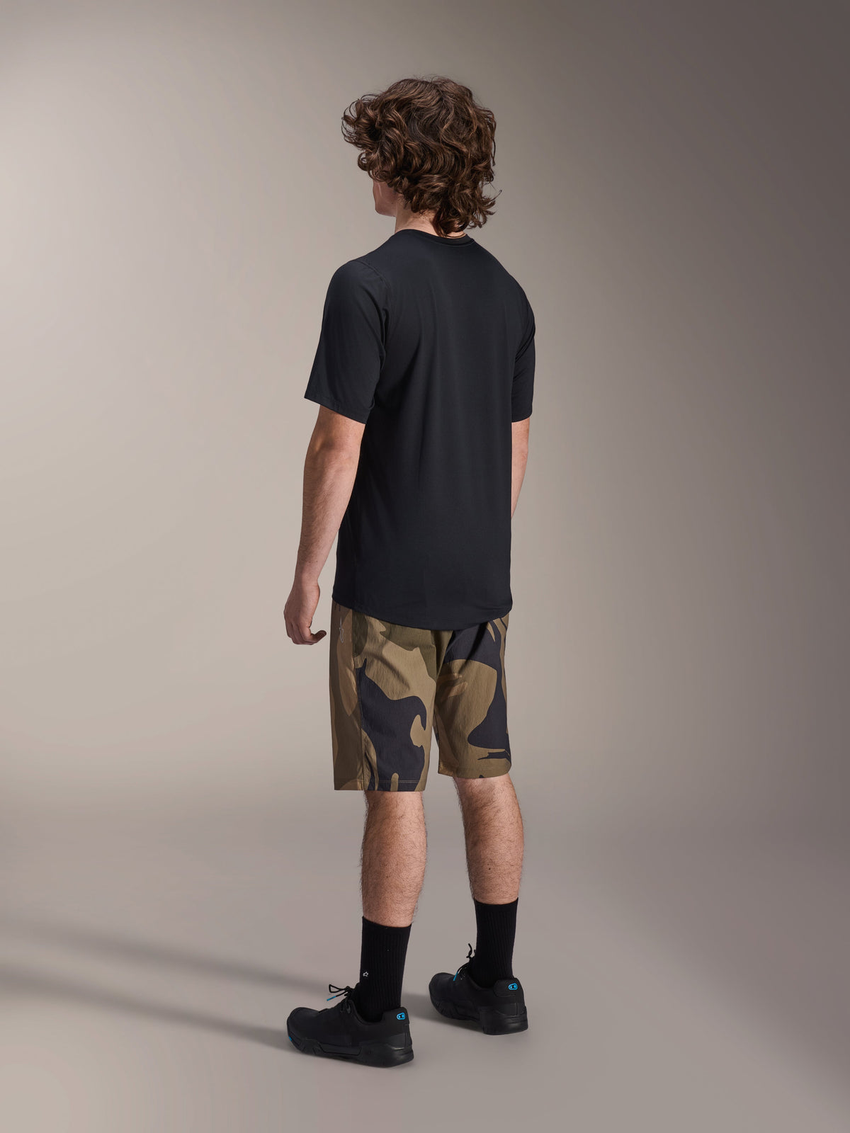 Alpinestars A-Dura Astar Short Sleeve Jersey in Black, viewed from the back, paired with camouflage pattern shorts and black athletic socks and shoes, casual MTB gear