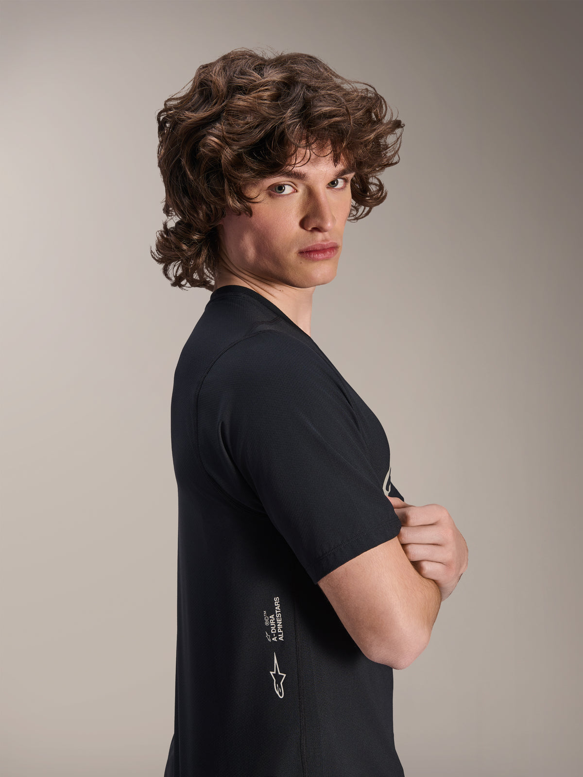 Alpinestars A-Dura Astar Jersey, Short Sleeve MTB Jersey, Black, male model posing in profile with arms crossed, featuring white Alpinestars branding on the lower side, casual athletic design for mountain biking.