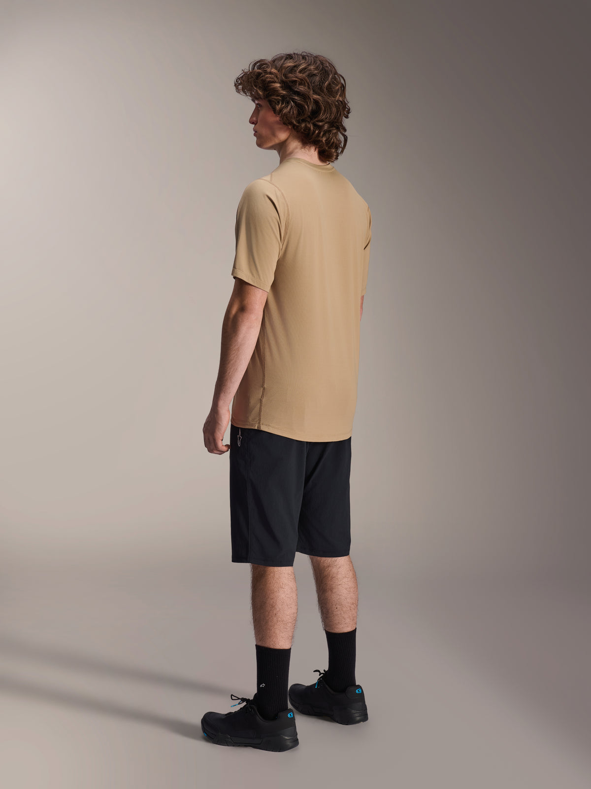 Alpinestars A-Dura Shorts, mountainbikeshorts, svarta, kombinerade med en beige kortärmad A-Dura-tröja och svarta cykelskor, med normal passform och slitstark konstruktion för terrängcykling, vy från sidan/bakifrån