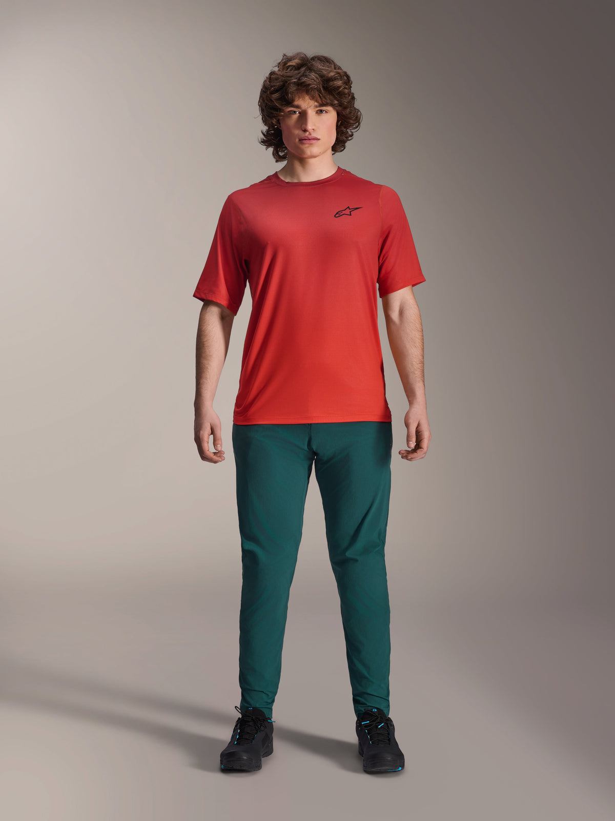 Alpinestars A-Dura Rise kortärmad tröja, Spicy Orange, bärs med mörkgröna byxor och svarta skor, svart Astars-logotyp på bröstet, funktionella mountainbikekläder för terrängkörning