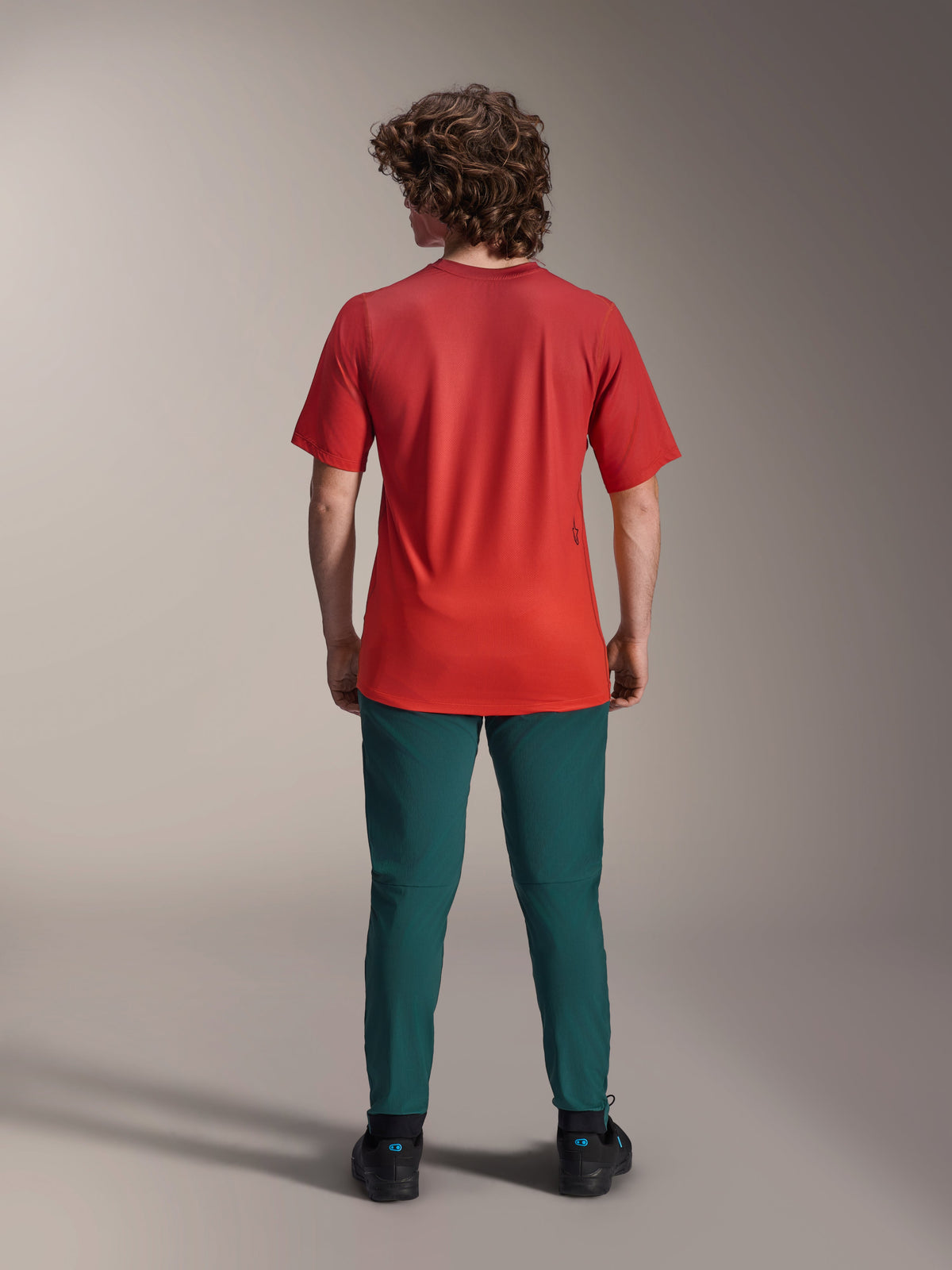 Alpinestars A-Dura Rise Jersey - kortärmad tröja, Spicy Orange, baksida på modell med mörkt blågröna byxor och svarta skor, förlängt ryggslut och liten screentryckt logotyp på ryggen, lättviktig MTB-utrustning