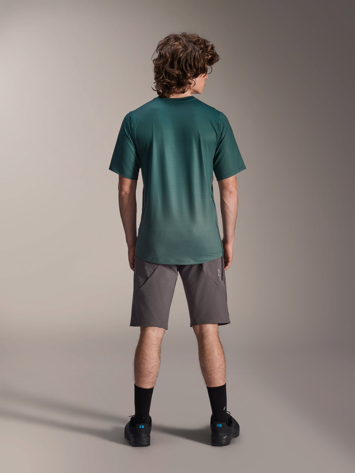 Alpinestars A-Dura Rise Jersey - kortärmad, Silver Pine-grön, ryggvy av en manlig modell som bär tröjan med grå shorts och svarta strumpor, med en förlängd bakre fåll och normal passform för mountainbikecykling