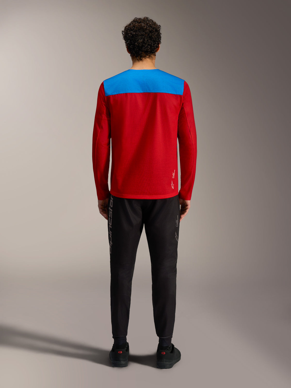 Alpinestars A-Dura Elite Long Sleeve Jersey 2.0, red and blue MTB jersey viewed from the back with black performance pants.