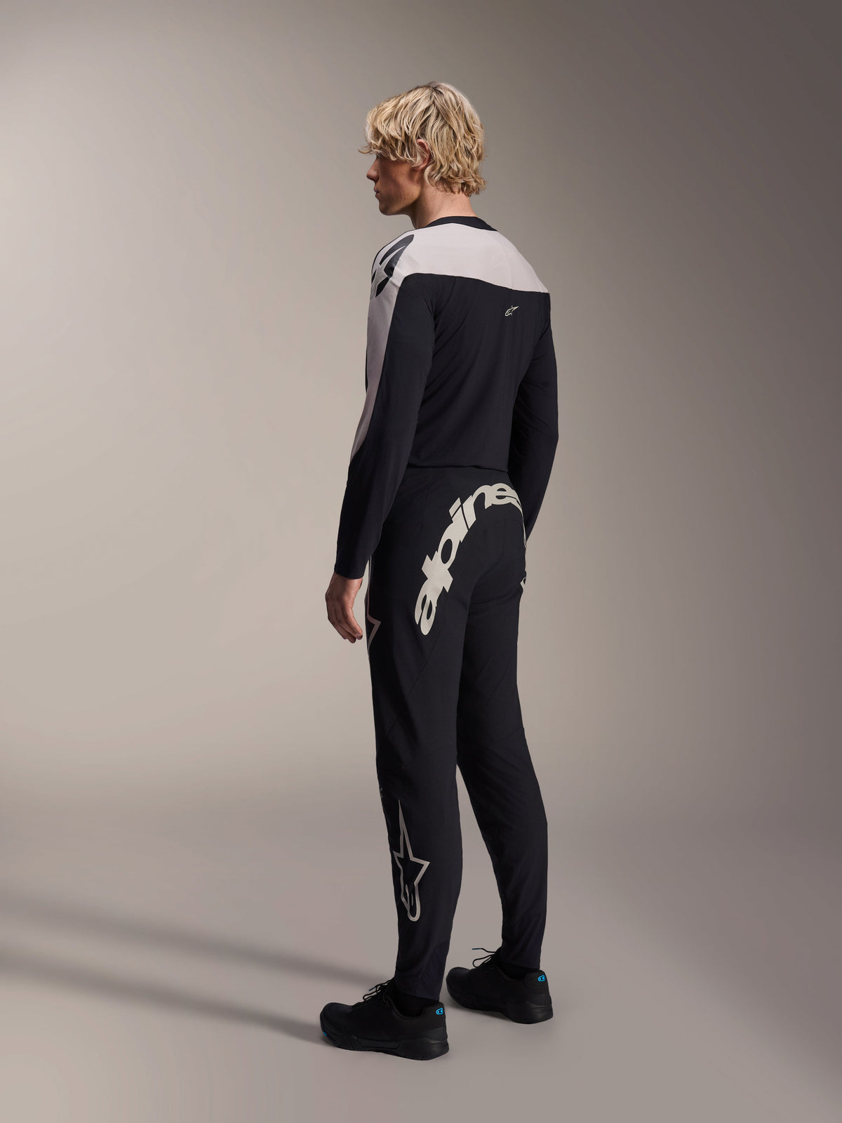 Alpinestars A-Supra Melt byxor, MTB-byxor, svarta, med ett stort vitt Alpinestars-ordmärke på bakoket och en stjärnlogotyp på benet, bärs av en modell med en matchande långärmad tröja och svarta skor, vy bakifrån