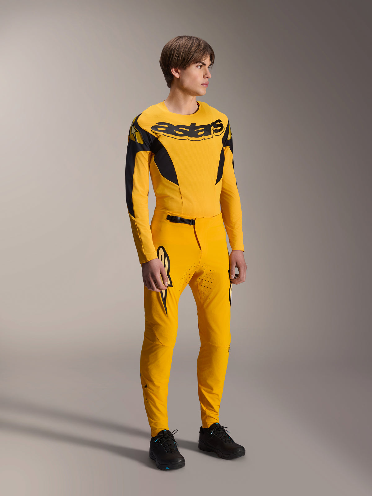 Manlig modell iförd Alpinestars Limited Edition A-Supra Melt Gold utrustningsset, gul långärmad MTB-tröja med framträdande svart logotyp på bröstet, matchande gula byxor med laserskuren ventilation och svarta detaljer, komplett racingställ för mountainbike.