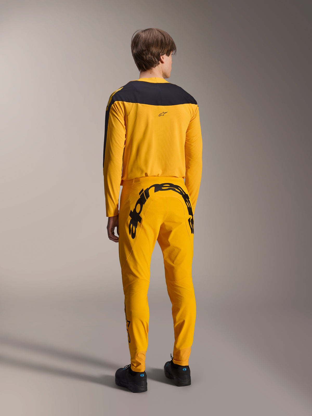 Alpinestars Limited Edition A-Supra Melt Gold-set, MTB-tröja och byxor, mörkgul och svart, vy bakifrån med stort Alpinestars-ordmärke över sätet och svart ok på tröjan, prestandakläder för mountainbike