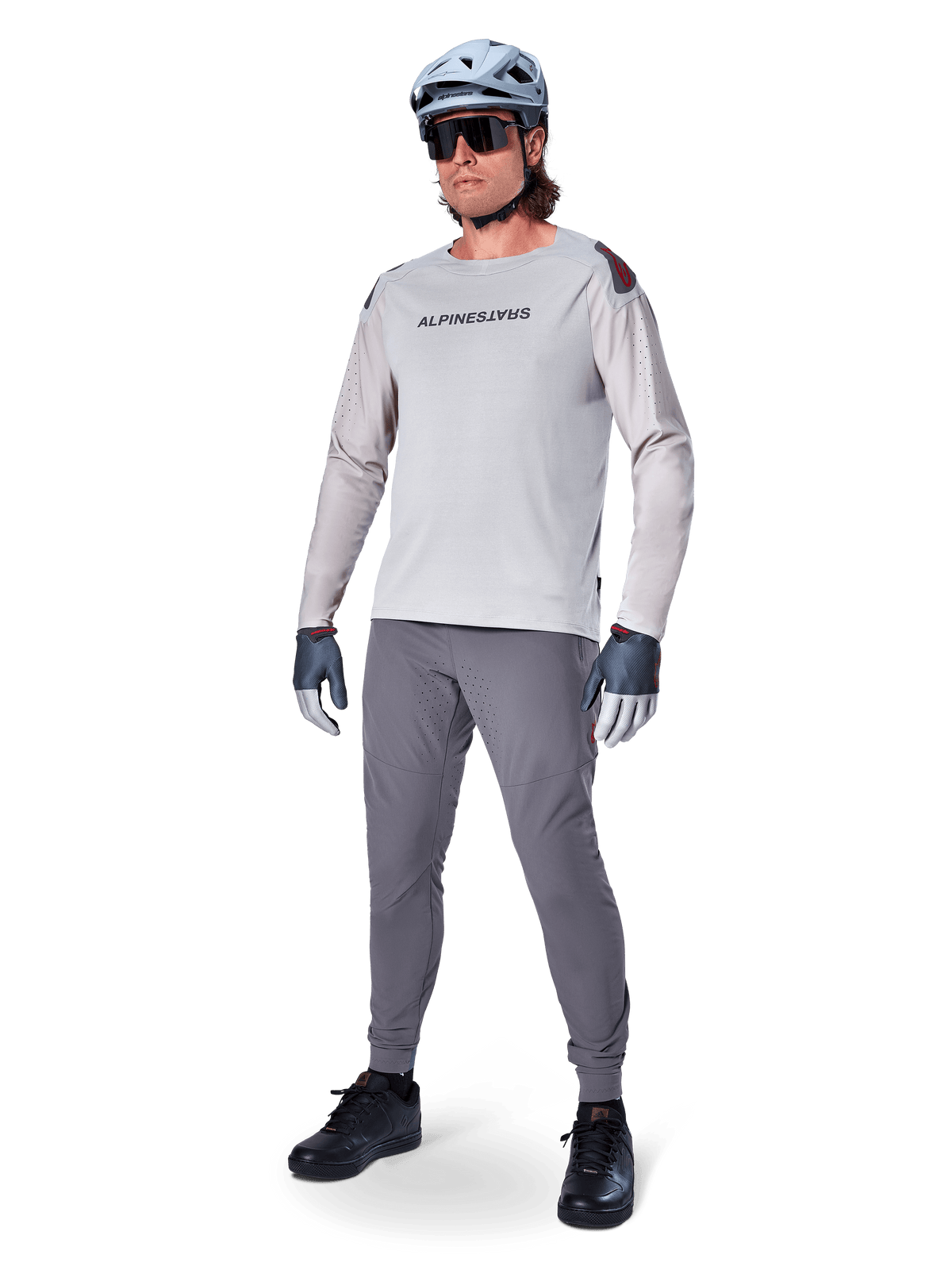 Alpinestars A-Aria Polartec Switch Jersey, långärmad MTB-tröja, ljusgrå, bärs tillsammans med mörkgrå mountainbike-byxor, hjälm och handskar, med laserperforerade ärmar och Alpinestars-logotyp på bröstet.
