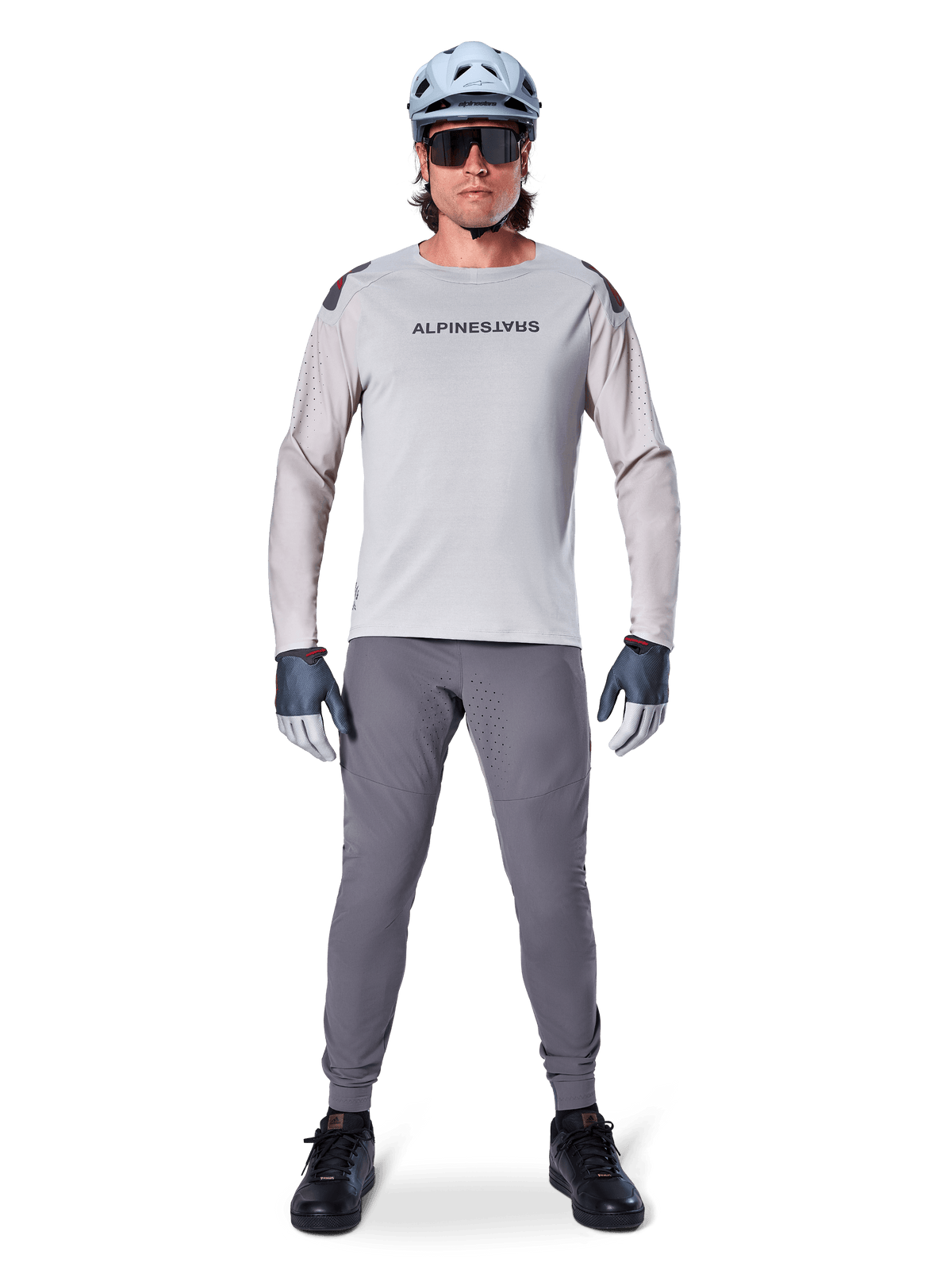 Alpinestars A-Aria Polartec Switch långärmad tröja, ljusgrå, bärs av en manlig mountainbikecyklist med mörkgrå MTB-byxor, ljusblå hjälm och solglasögon, med logotyp på bröstet och laserperforerad ventilation på ärmarna, komplett outfit för terrängkörning