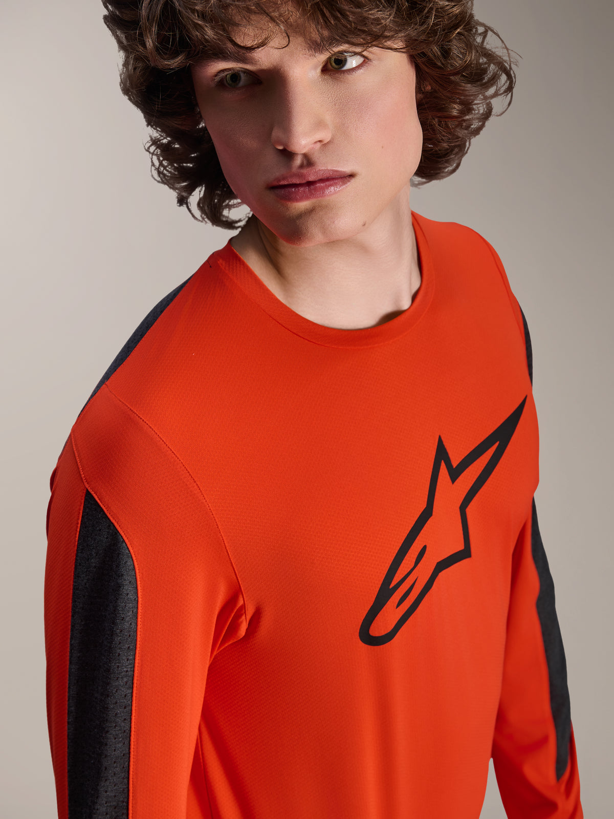 Alpinestars A-Dura Insert Astar Long Sleeve Jersey, Spicy Orange MTB jersey with large black Astar logo on chest, dark grey sleeve panels, worn by a model in a close-up studio shot, textured technical fabric.
