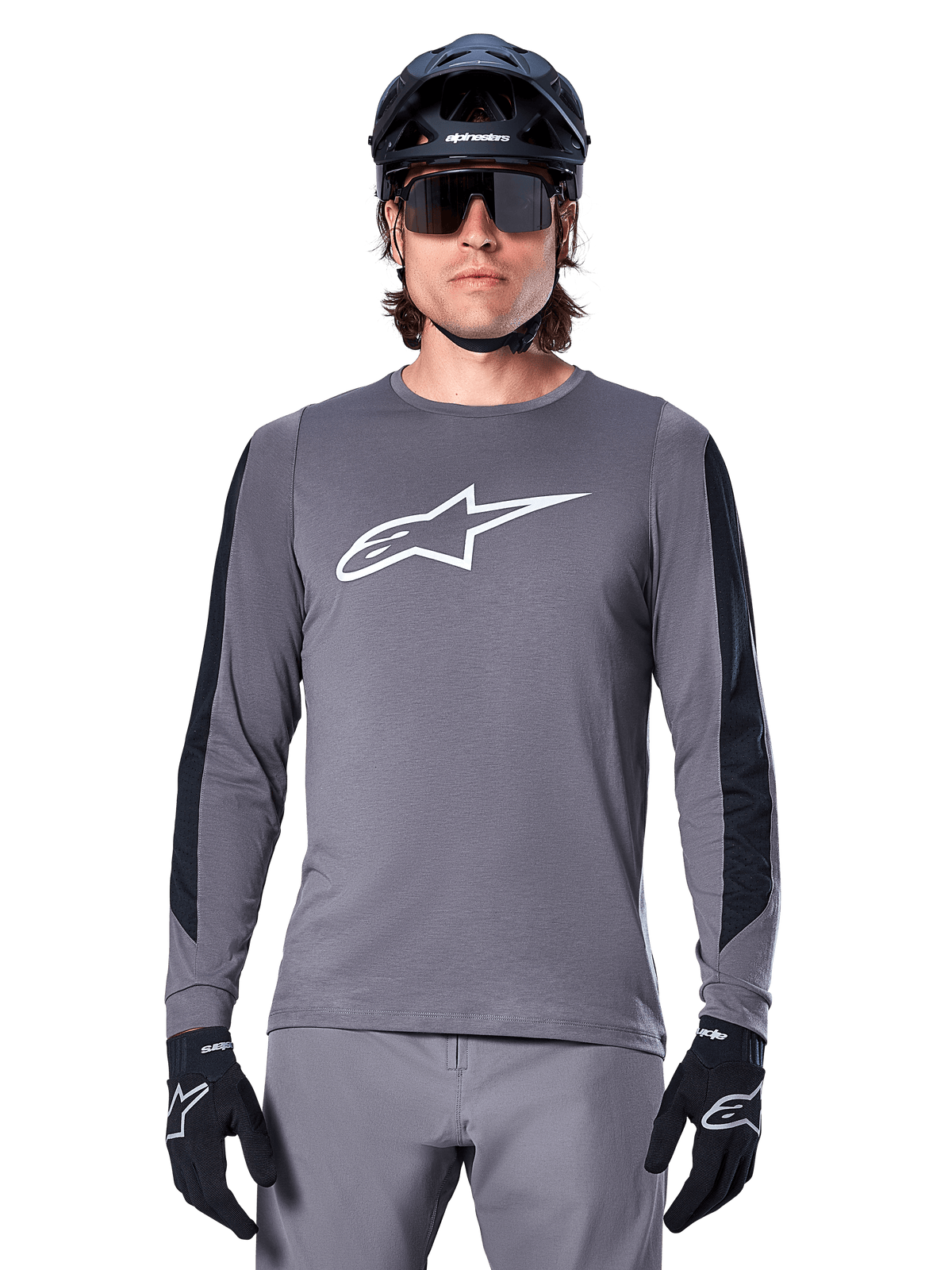 Alpinestars A-Dura Dri Astar långärmad tröja, mörkgrå, med en stor vit Astar-logotyp på bröstet och svarta meshpaneler på ärmarna, bärs av en cyklist med en svart mountainbikehjälm och sportglasögon, MTB-cykelkläder