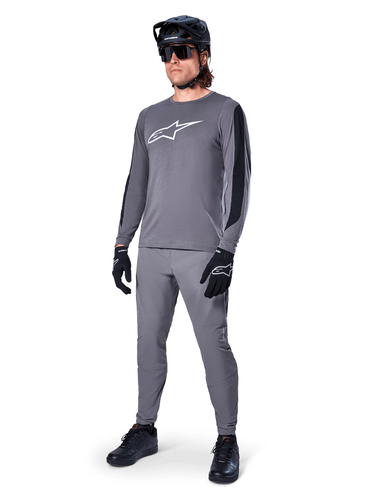 Alpinestars A-Dura Dri Astar-tröja, långärmad MTB-tröja, mörkgrå med vit bröstlogotyp, svarta meshpaneler på ärmarna, bärs med matchande gråa byxor, svart hjälm och handskar, högpresterande mountainbike-kläder