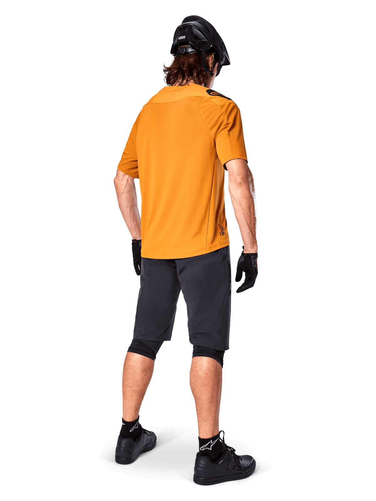Alpinestars A-Aria Polartec Switch-tröja, kortärmad MTB-tröja, mörkt guld, baksida av modell som bär mörkgrå mountainbike-shorts, svart hjälm och handskar, tekniska cykelkläder för terrängstigar