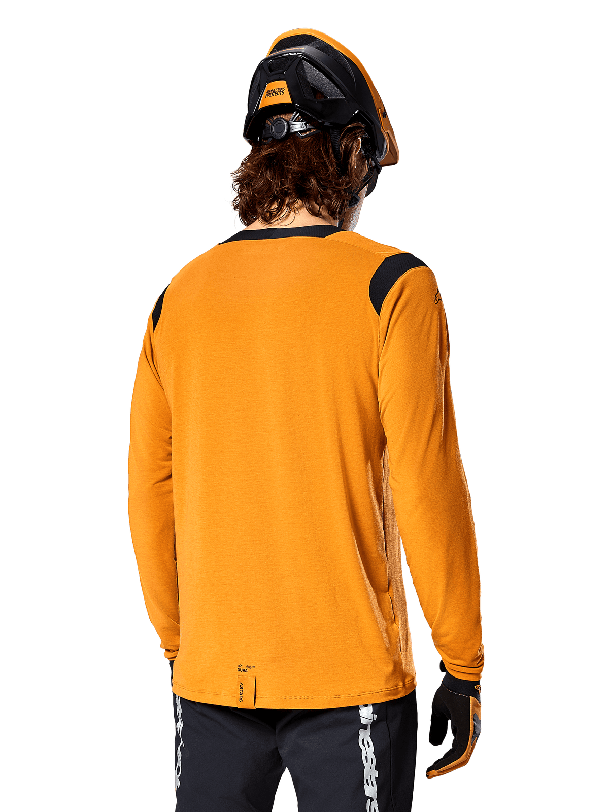 Alpinestars A-Dura Dri Wool långärmad tröja i Dark Gold, sedd bakifrån på en cyklist med mountainbikehjälm och handskar, svarta meshpaneler på axlarna och ett längre ryggslut, tekniska cykelkläder för trailcykling