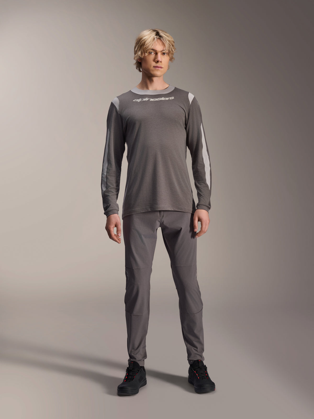 Alpinestars A-Dura Dri Wool långärmad jersey, mörkgrå, bärs av modell med matchande grå byxor och svarta skor, vit Alpinestars-logotyp på bröstet, ljusgrå meshpaneler på axlar och ärmar, teknisk mountainbike-utrustning