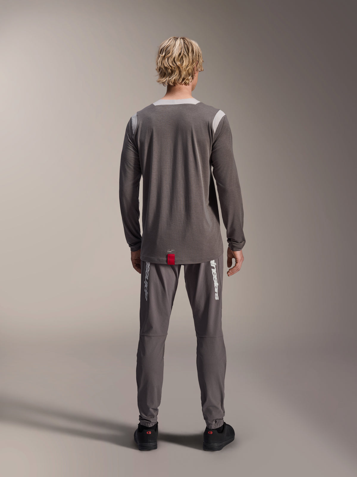 Alpinestars A-Dura Dri Wool Jersey - långärmad, mörkgrå, baksida på modell, med ljusgrå meshpaneler på axlar och krage, längre bakstycke med en liten röd märkesetikett, bärs med matchande grå cykelbyxor