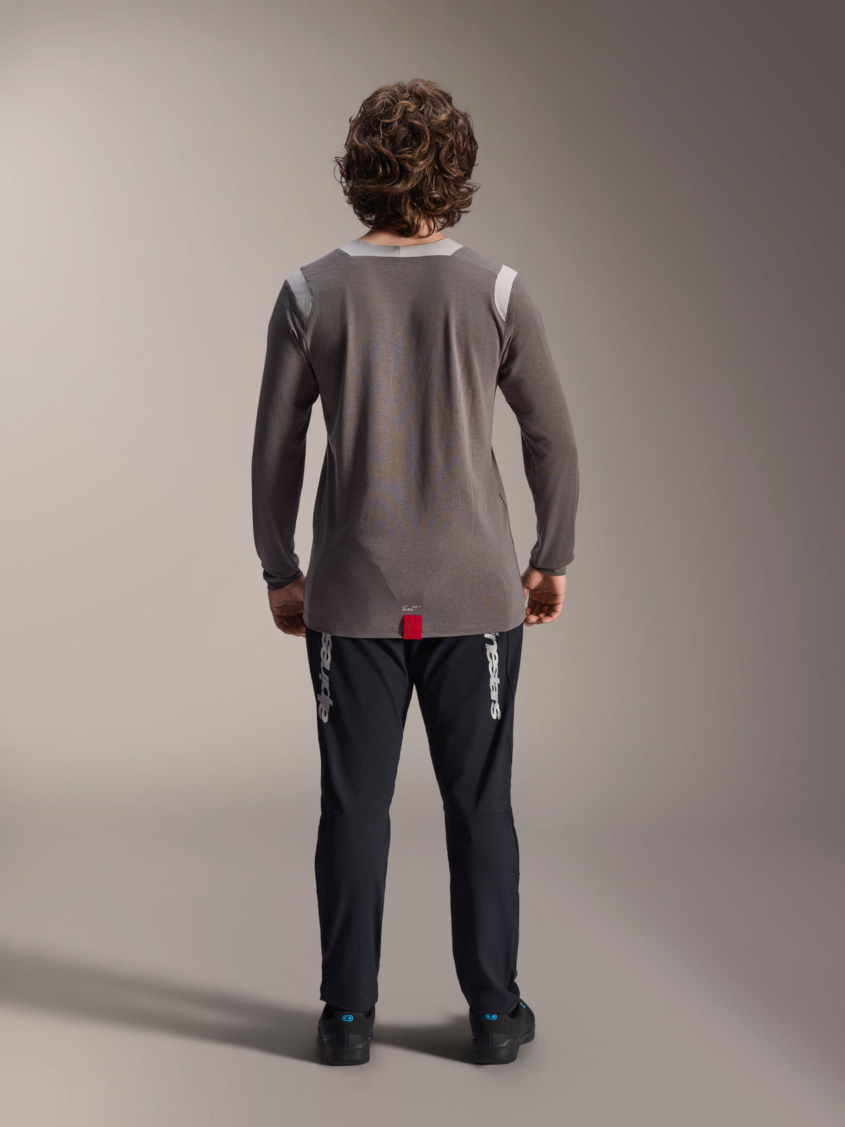 Alpinestars A-Dura Elite-byxor och A-Dura Dri Wool långärmad tröja, svarta byxor med vit logotyp, grå teknisk tröja, vy bakifrån av mountainbike-outfit, slitstarka cykelkläder för terrängkörning