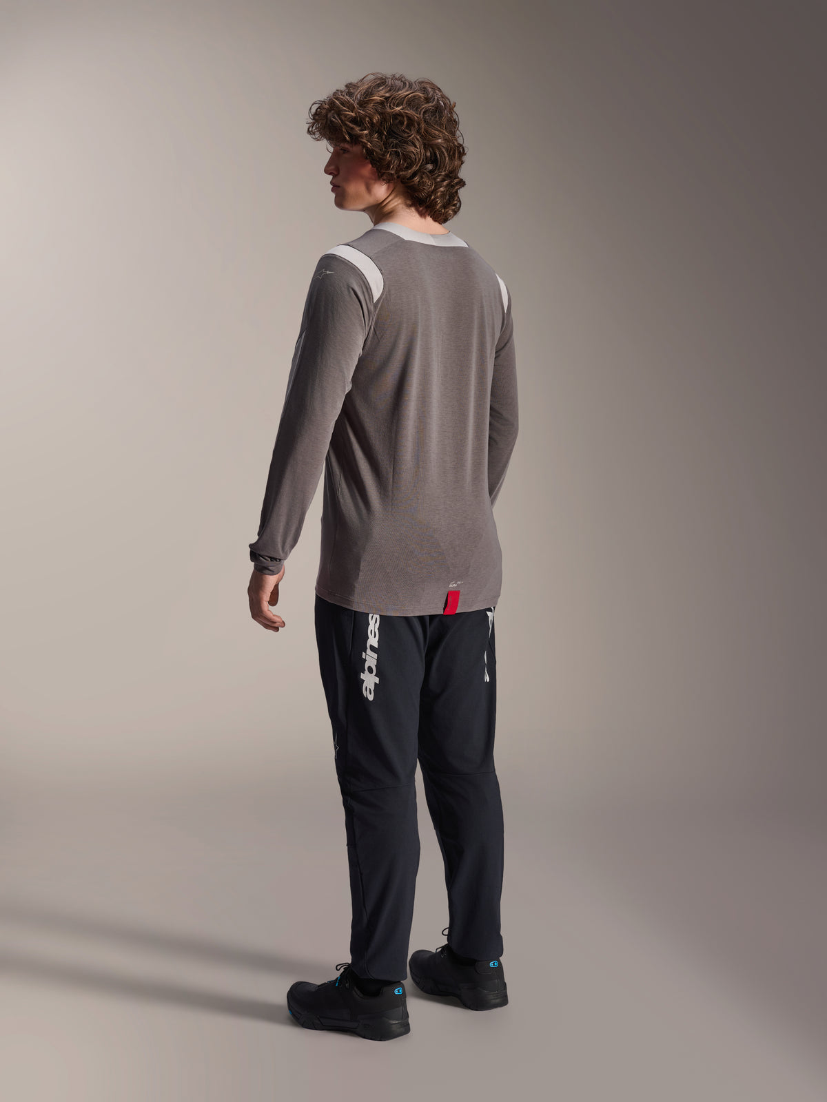 Alpinestars A-Dura Dri-Wool långärmad tröja i grått tillsammans med A-Dura Elite-byxor i svart, ryggvy av modellen, vit Alpinestars-logotyp på benet, teknisk mountainbike-utrustning för terrängkörning