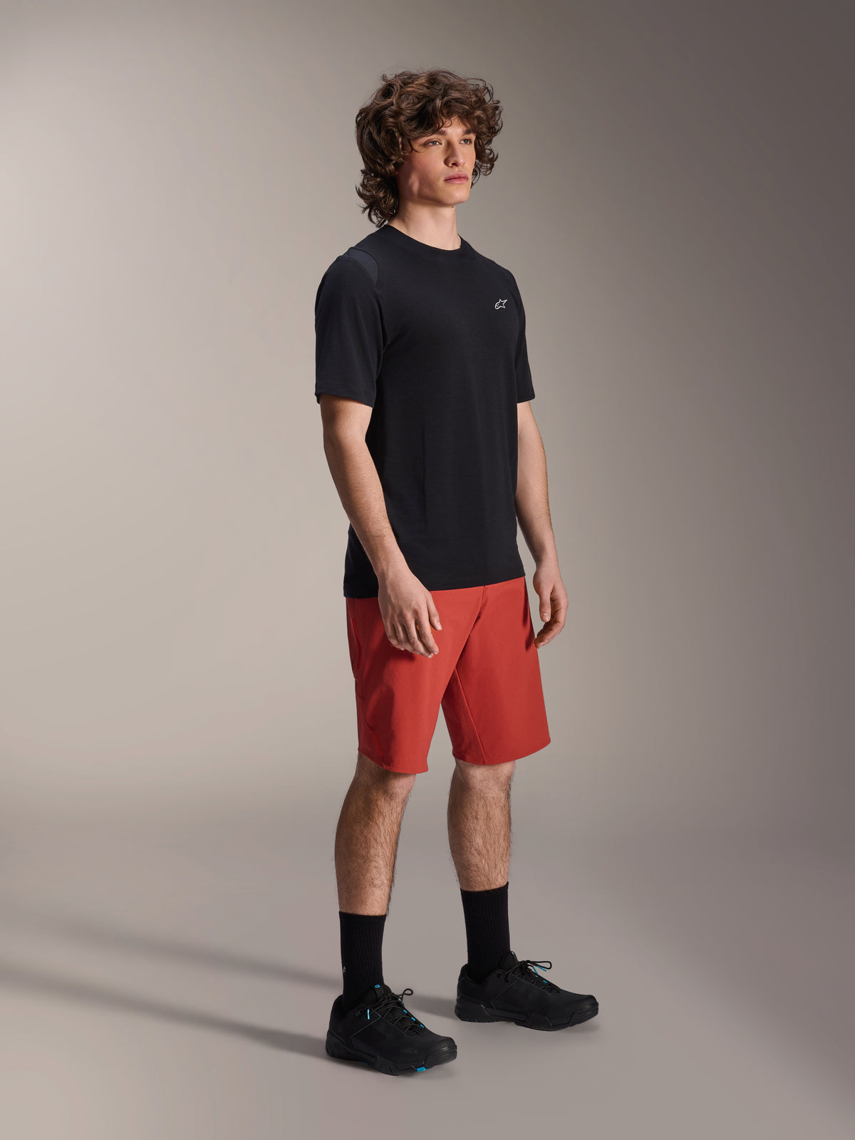 Manlig modell iklädd Alpinestars A-Dura Elite-shorts i Dark Orange och A-Dura Dri Wool kortärmad tröja i svart, prestationskläder för mountainbike, kombinerat med svarta strumpor och skor, atletisk design för terrängcykling.
