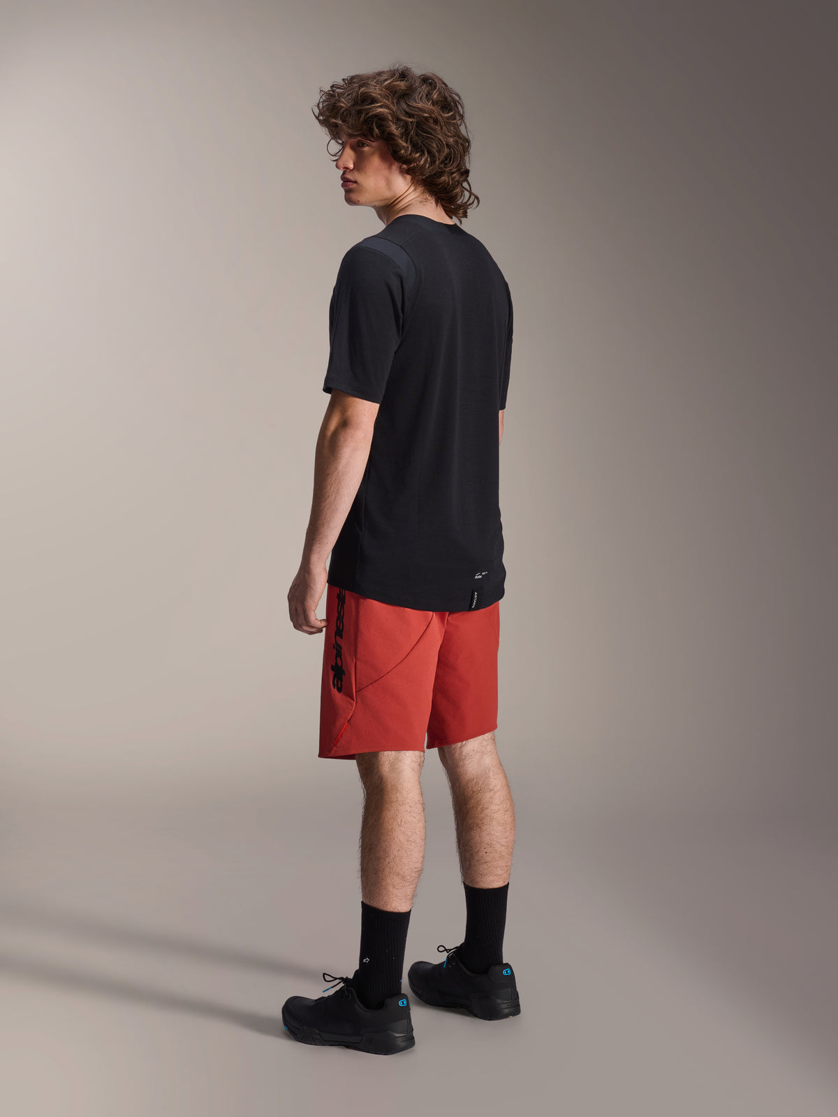 Alpinestars A-Dura Elite Shorts, mountainbike-shorts, mörkorange, bärs med en svart kortärmad tröja och svarta mountainbike-skor, vy från sidan bakifrån på modell som framhäver prestandapassform och logotyp
