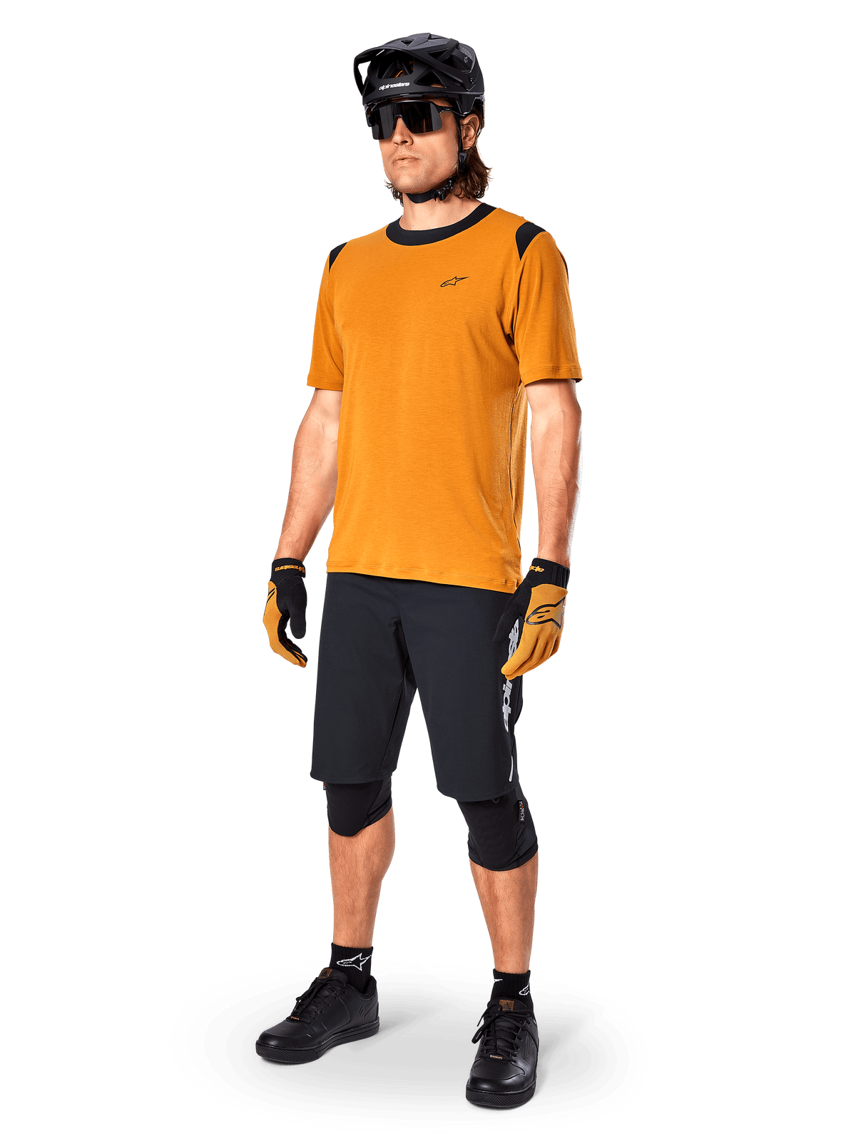 Manlig modell bär Alpinestars A-Dura Dri Wool Jersey - Short Sleeve i Dark Gold, mountainbiketröja med svarta detaljer på axlar och krage, kombinerad med svarta MTB-shorts, svart hjälm och solglasögon, teknisk cykelutrustning för terrängkörning
