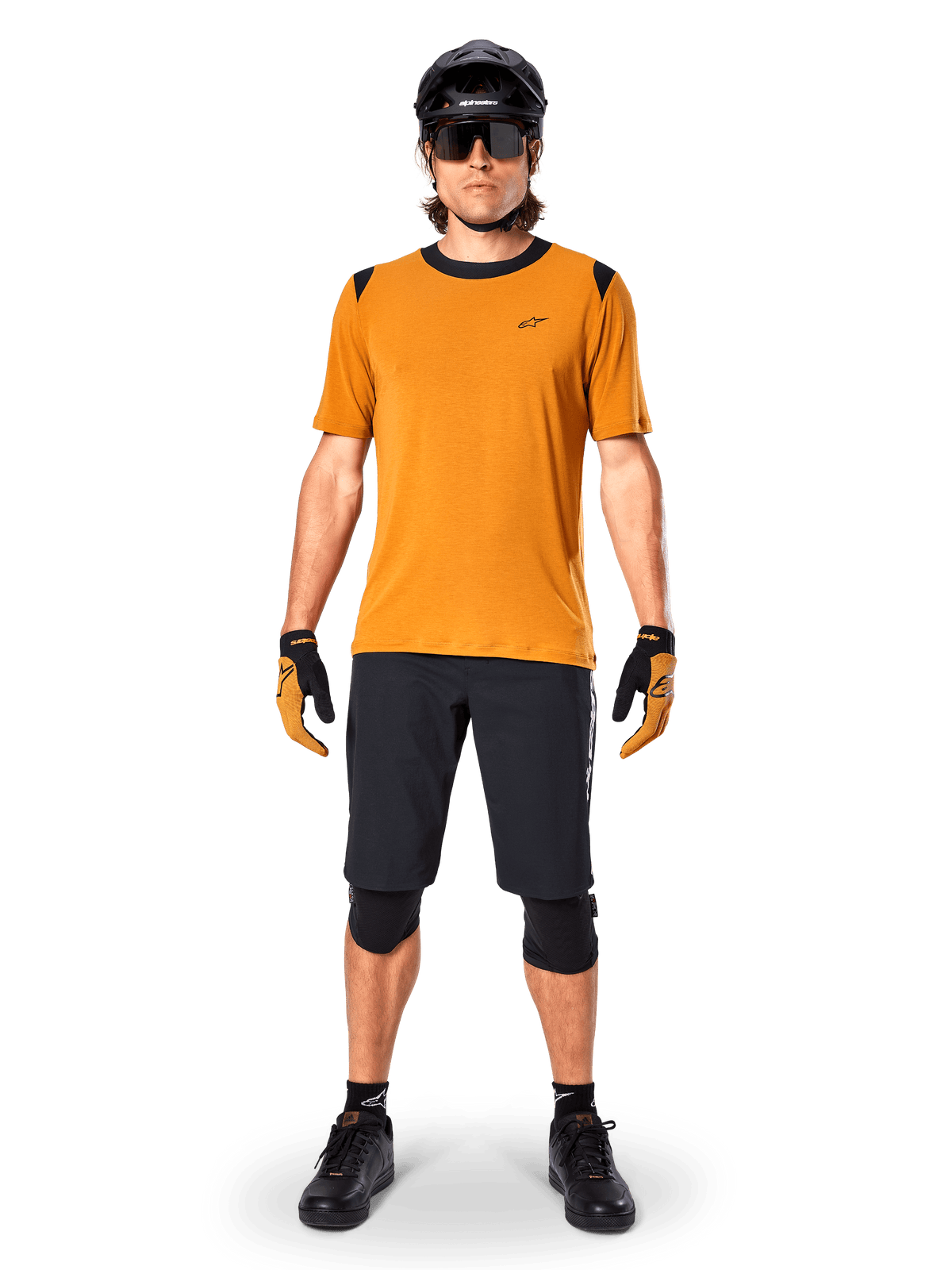Alpinestars A-Dura Dri Wool kortärmad tröja i Dark Gold, mountainbike-tröja buren med svarta shorts och skyddsutrustning, senapsgult tyg med svart krage och axeldetaljer, funktionella cykelkläder för stigcykling.