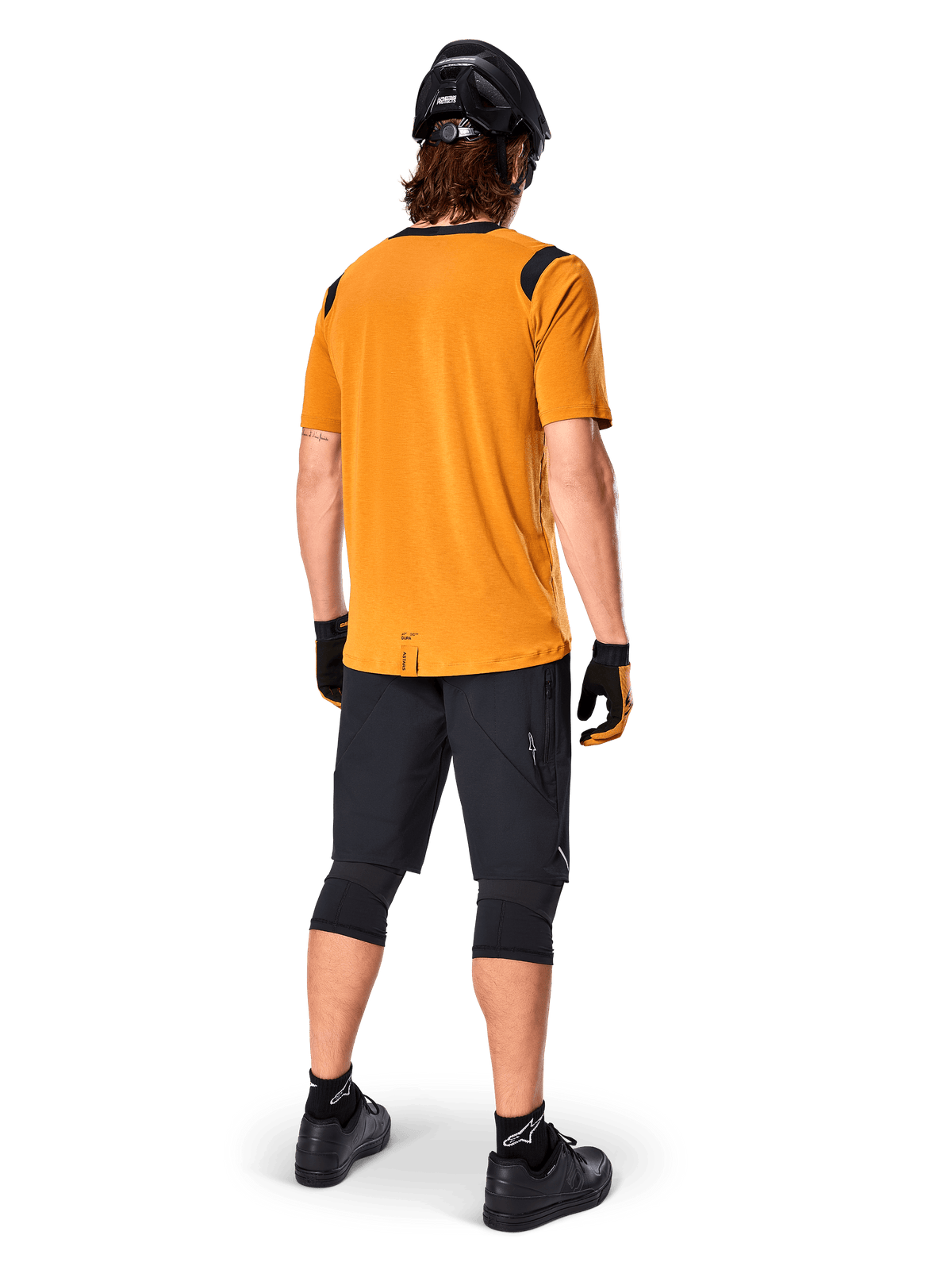 Alpinestars A-Dura Dri Wool kortärmad tröja, cykeltröja, Dark Gold, baksida av mountainbikecyklist i senapsgul tröja med svarta axeldetaljer i mesh, kombinerat med svarta shorts, knäskydd, svart hjälm och handskar, teknisk utrustning för terrängcykling