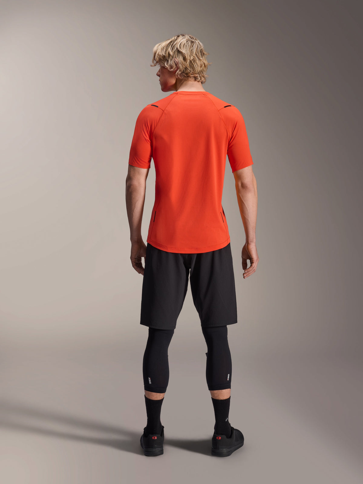 Alpinestars A-Aria Astar tröja, kortärmad MTB-tröja, Spicy Orange, vy bakifrån som visar prestandapassform och förlängt ryggslut, kombinerad med svarta cykelshorts och leggings