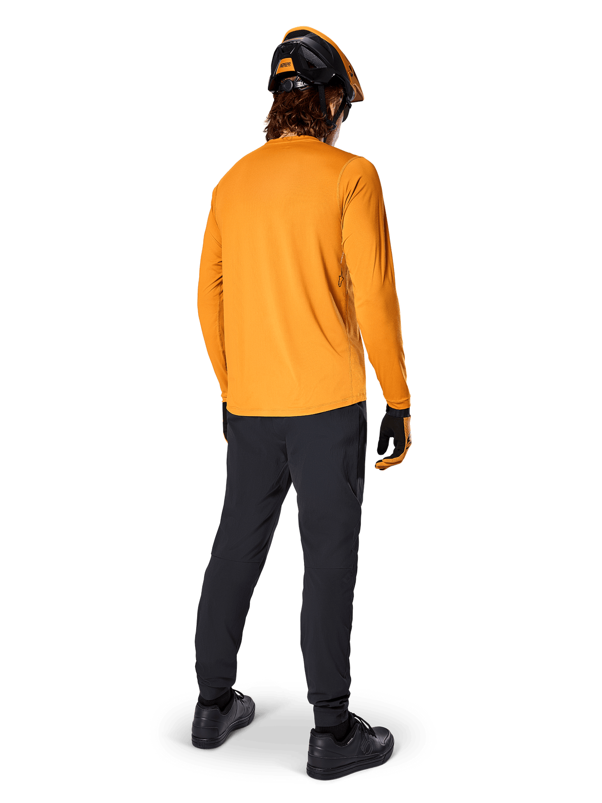 Mountain bike rider seen from behind wearing the Alpinestars A-Dura Rocker Long Sleeve Jersey in Dark Gold, black pants, orange and black helmet, and black shoes, coordinated performance MTB gear for trail riding