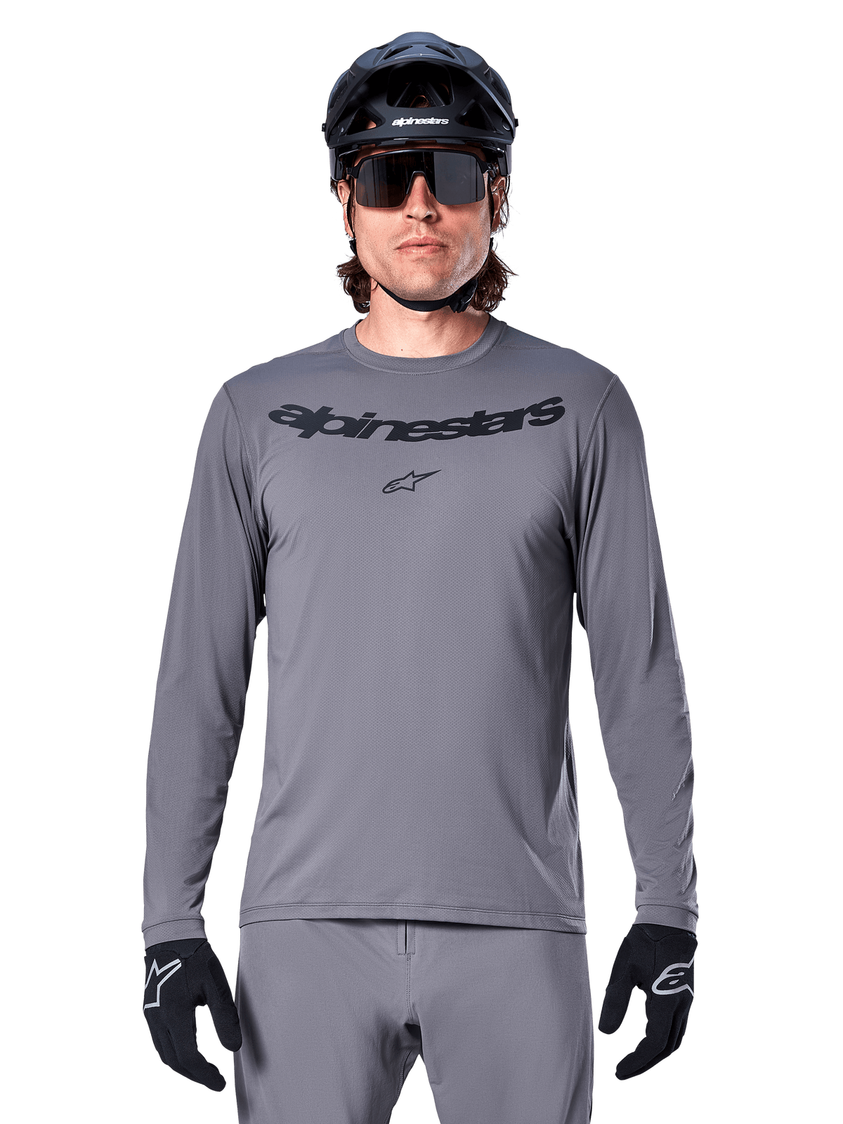 Alpinestars A-Dura Rocker långärmad tröja, mörkgrå MTB-tröja med svart ordmärke på bröstet, bärs av en manlig cyklist tillsammans med gråa byxor, svart hjälm och handskar, designad för terrängcykling
