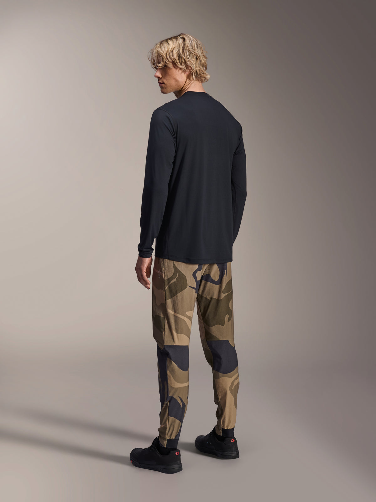 Alpinestars A-Dura Astar Long Sleeve Jersey, Black, back view on a model, paired with camouflage pants, casual MTB performance gear with a drop tail hem and regular fit