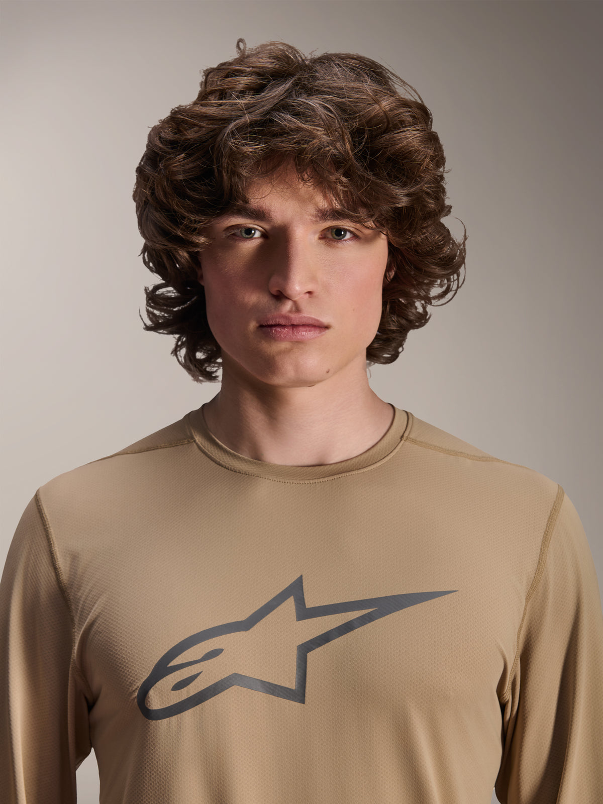 Alpinestars A-Dura Astar långärmad tröja, ljusbrun, bärs av manlig modell, stor Astars-logotyp på bröstet, jacquardvävd textur, avslappnad mountainbike-utrustning