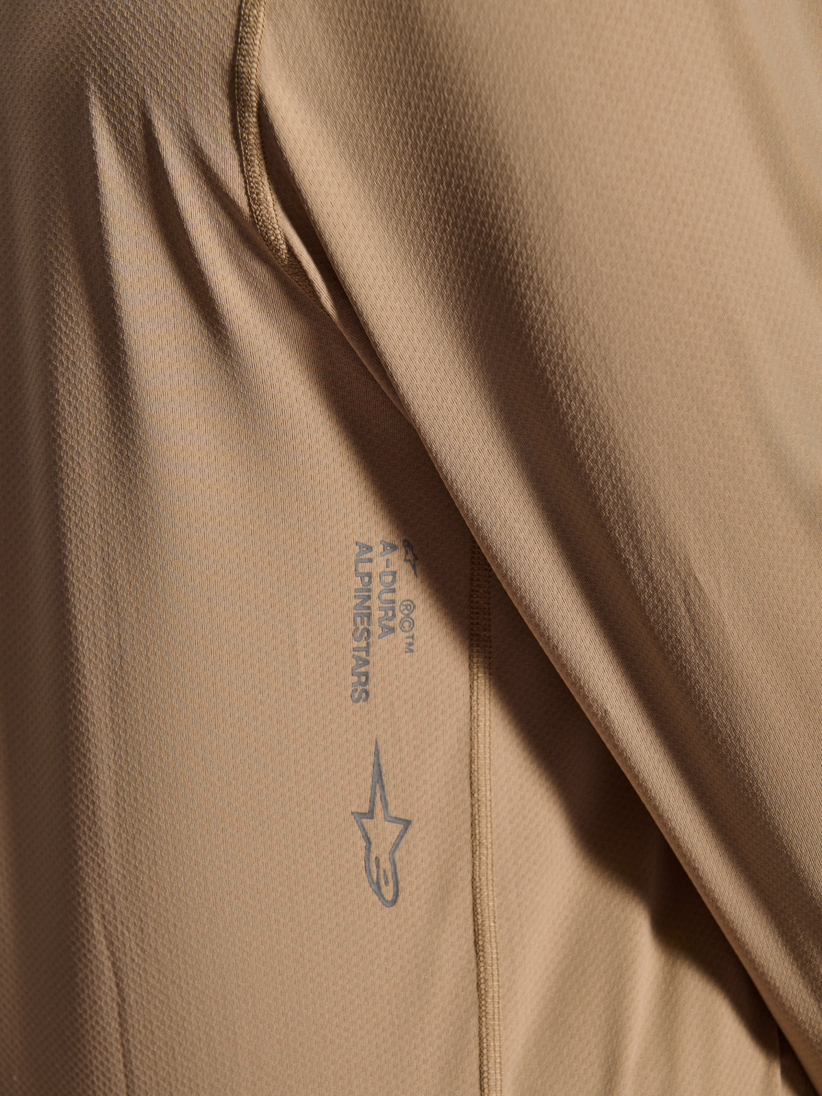 Alpinestars A-Dura Astar långärmad tröja, MTB-cykeltröja, brun, närbild som visar jacquard-tygets struktur, tryckt Astars-logotyp och A-Dura-ordmärke, teknisk mountainbike-utrustning