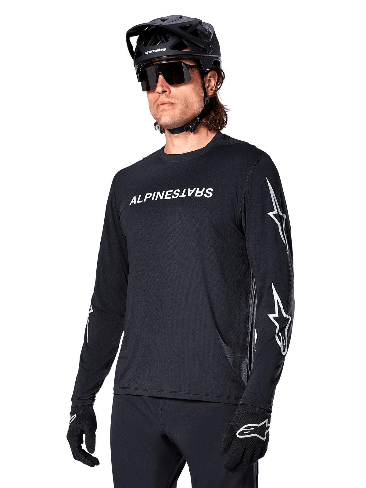 Manlig cyklist i Alpinestars A-Dura Switch långärmad tröja, svart med vit ordmärkeslogotyp och stjärnlogotyper på ärmarna, kombinerad med svart MTB-hjälm och solglasögon, högpresterande cykelutrustning för terrängcykling